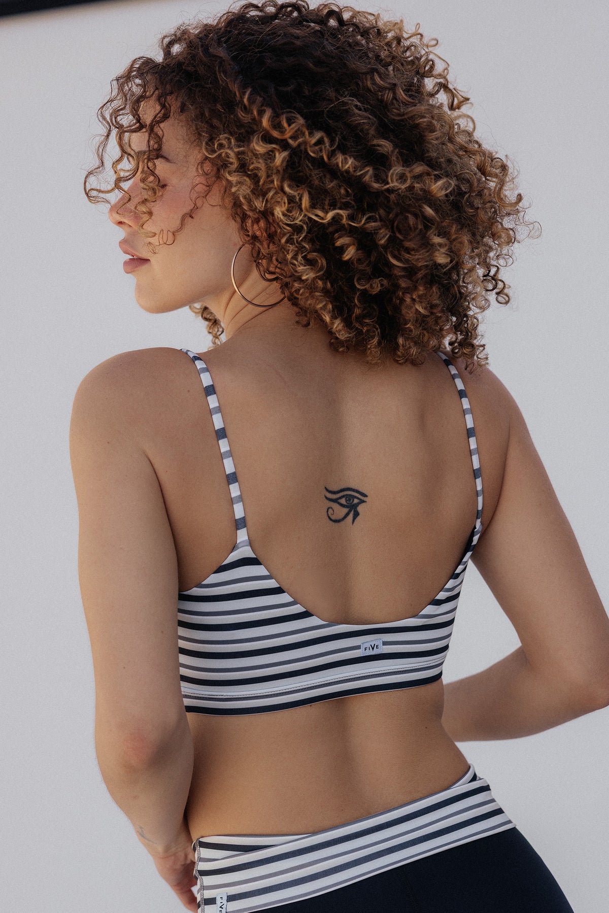 women, with curly brown hair is shown from the back wearing a black and white striped sports bra and matching bottoms against a plain white background.