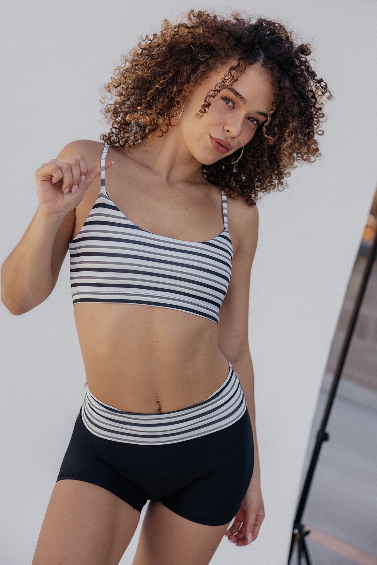 women, modeling a matching two-piece activewear set featuring a black and white horizontally striped top and solid black bottoms with a striped waistband.