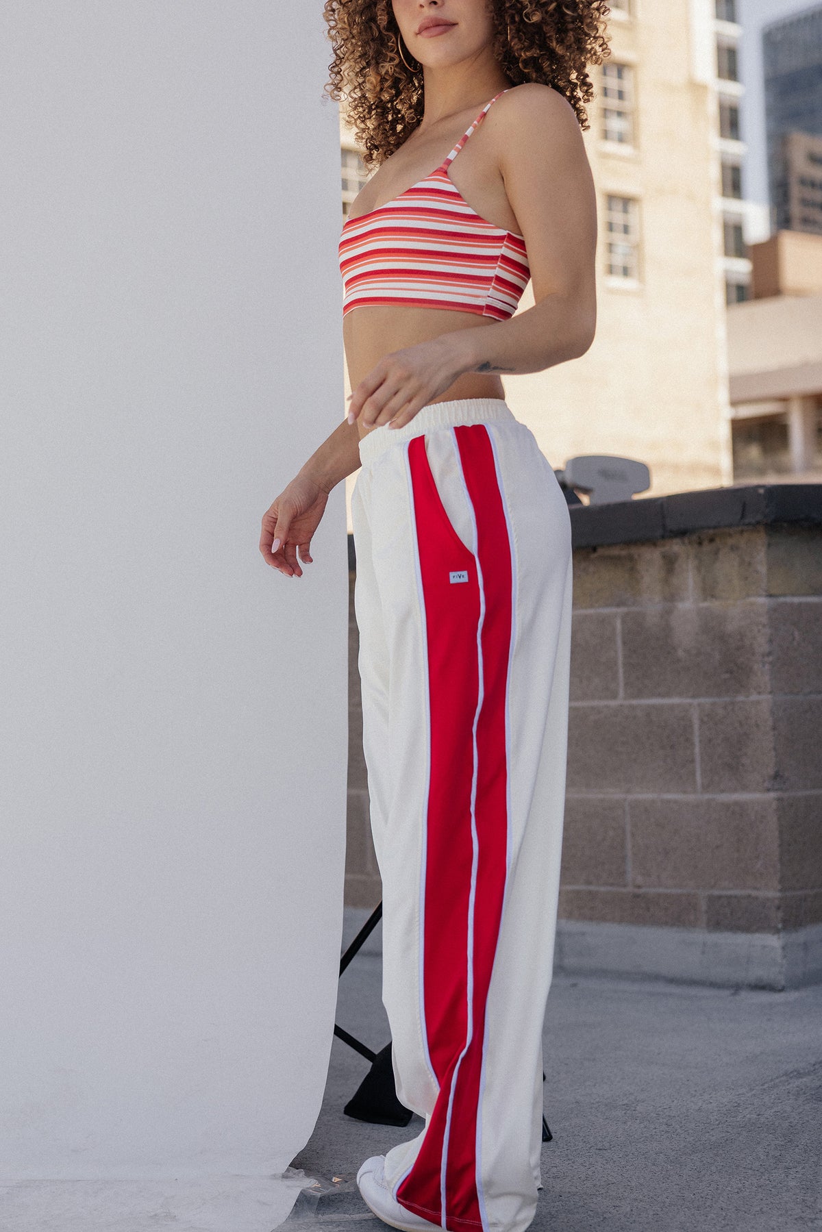 women, A model wearing a red and white striped crop top and matching red and white wide-leg track pants, standing outdoors next to a white studio backdrop.