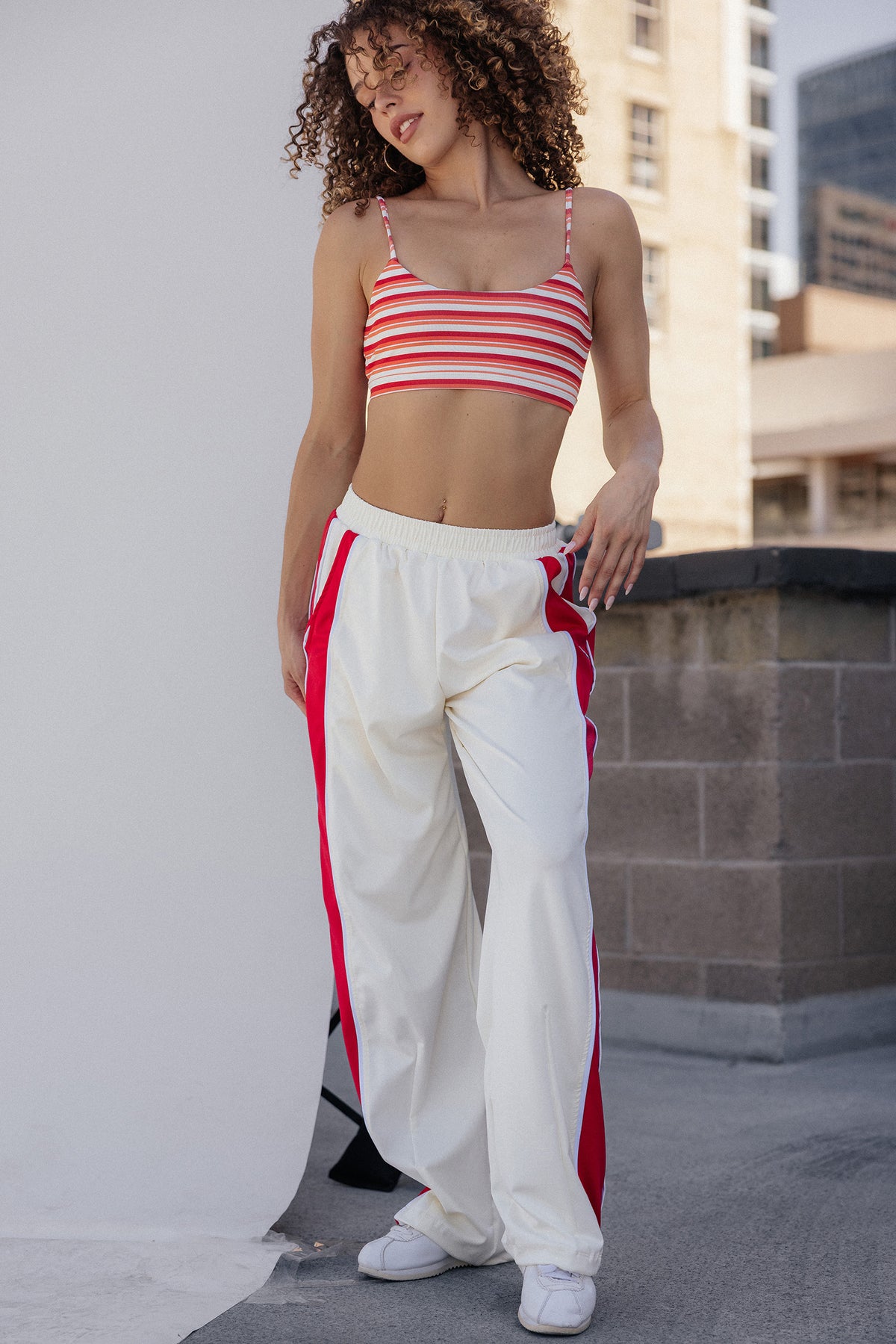 women, A woman modeling a red and white striped crop top with matching red side stripes on white wide-leg sweatpants, standing on a rooftop with a city background.