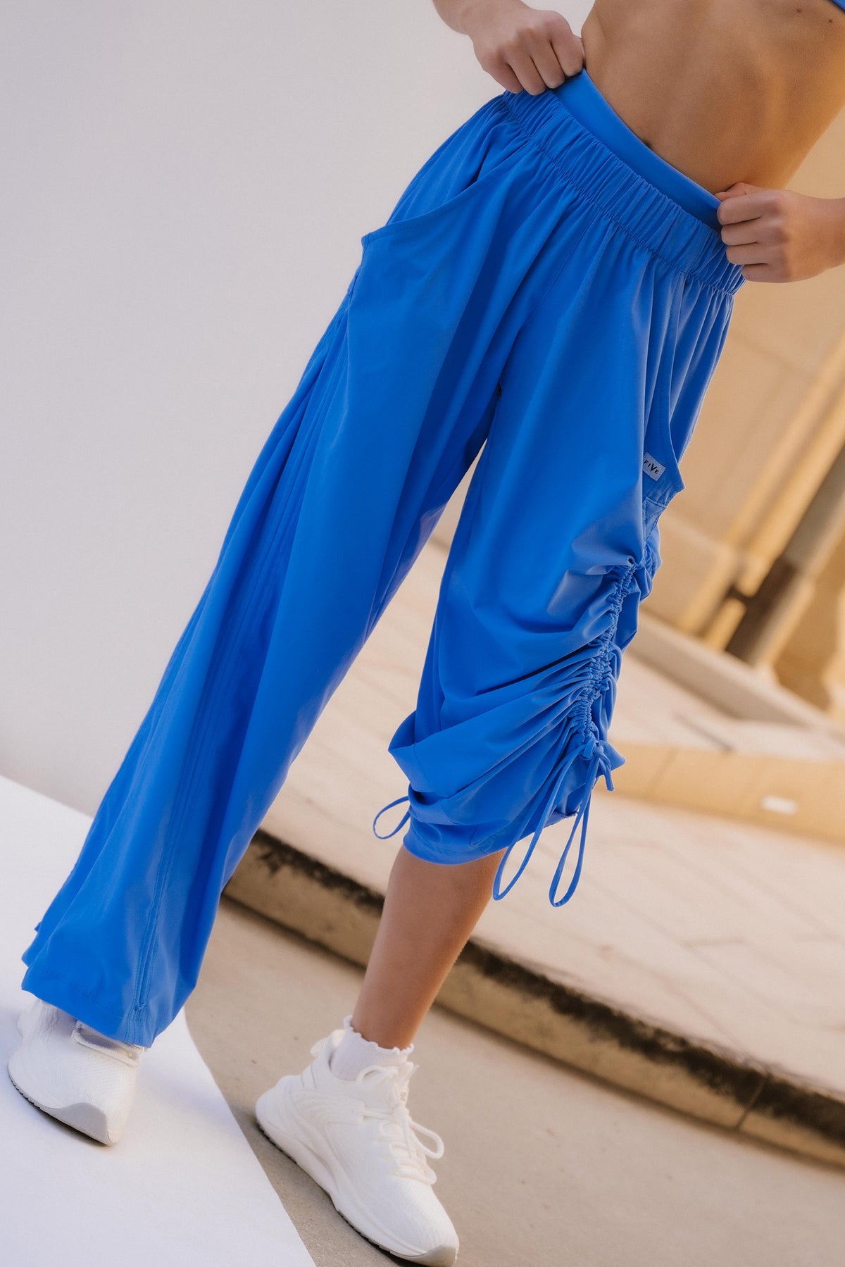 kids, A model wearing bright blue ruched ruched sweatpants, styled with a matching blue sports bra and white sneakers, standing on a white platform.