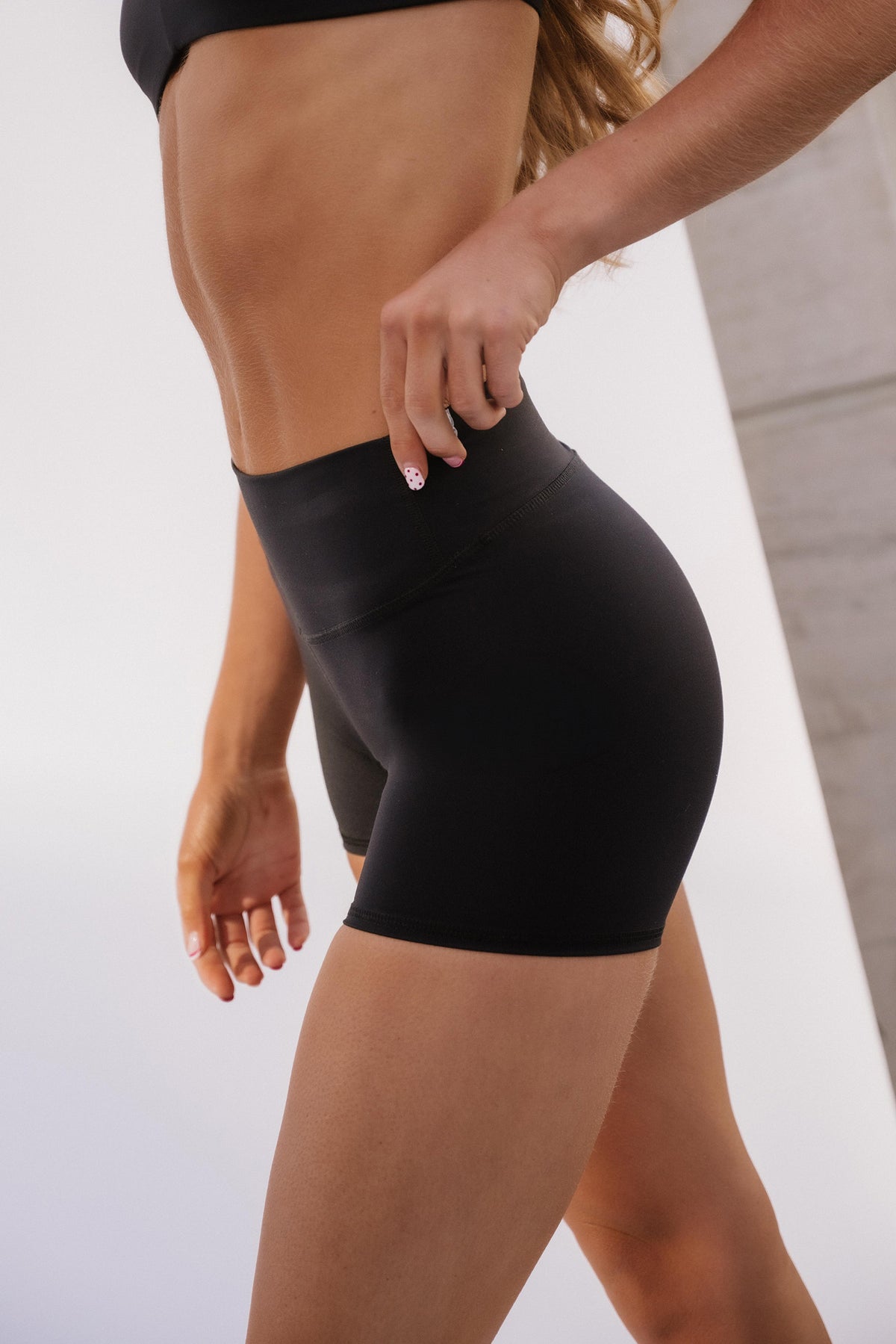 teen, Close-up of a model wearing black high-waisted athletic shorts, showing the fit and waistband detail.
