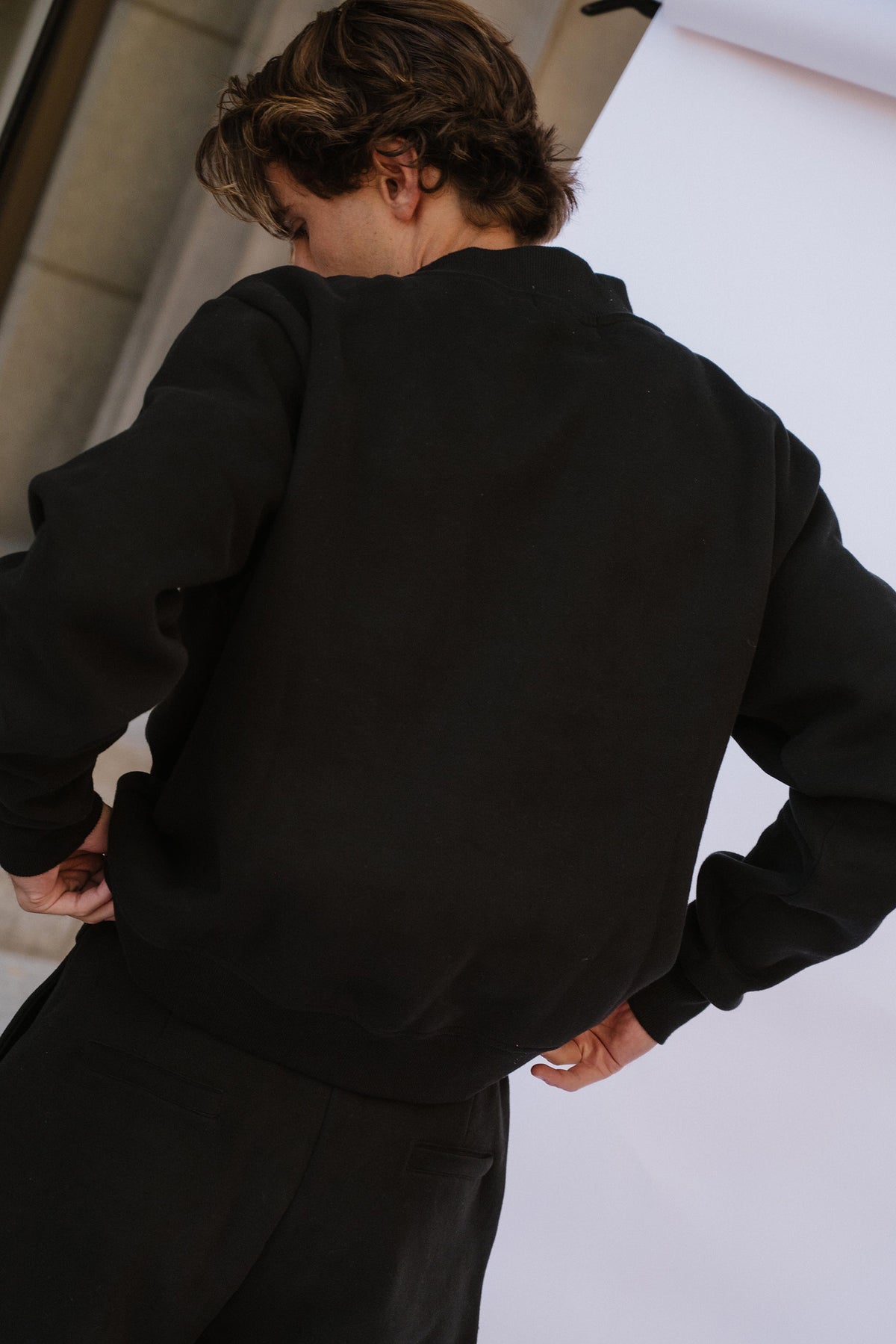 mens, A person shown from behind wearing a black crewneck sweatshirt and black pants, standing against a white backdrop.