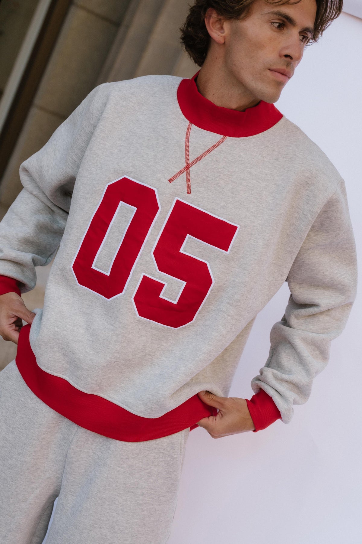 mens, A man wearing a light gray heather crewneck sweatshirt with bold red ribbed trim and large red '05' lettering on the front, paired with matching gray sweatpants.