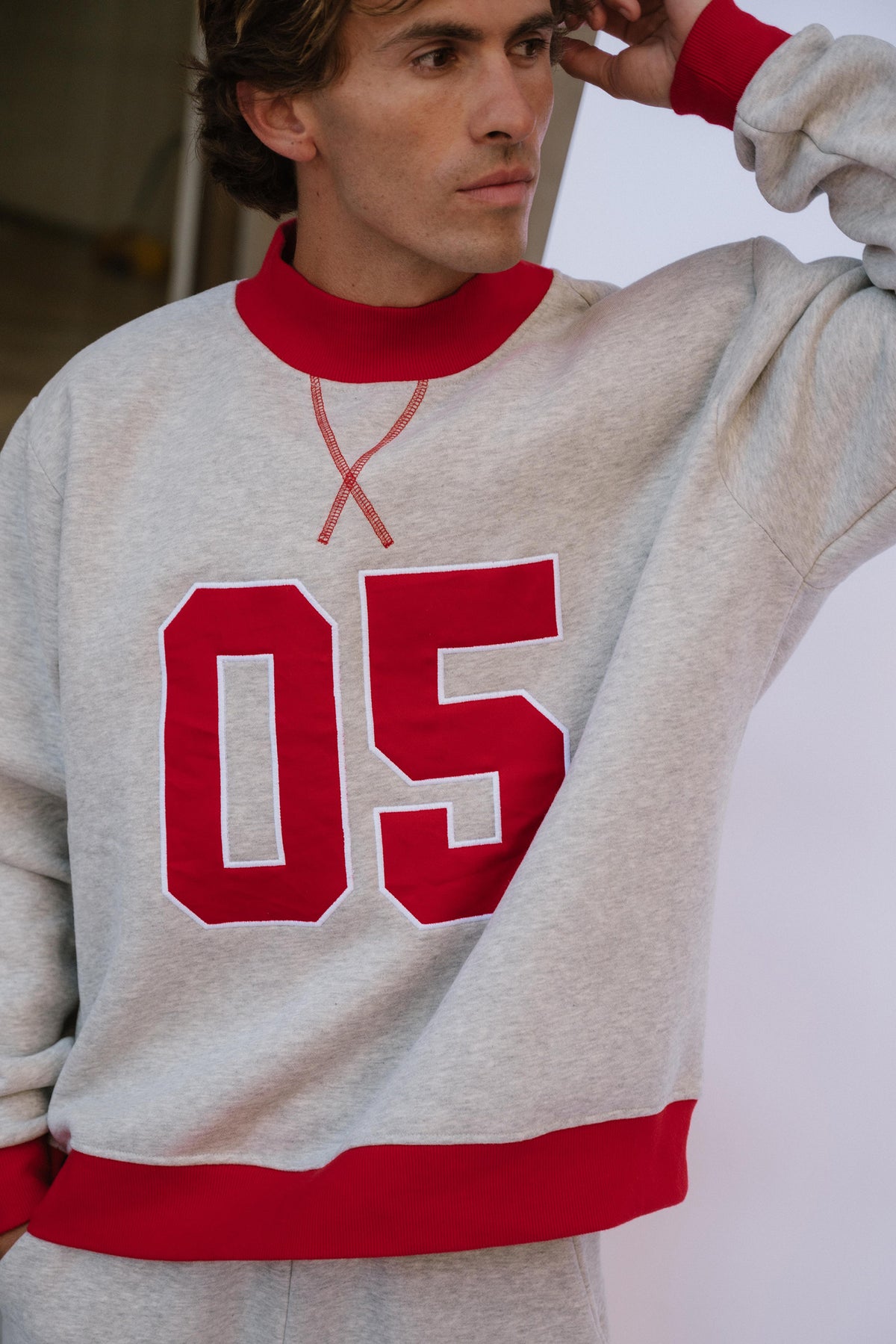mens, A man wearing a light heather gray crewneck sweatshirt with bold red ribbed trim and large red '05' lettering on the front.