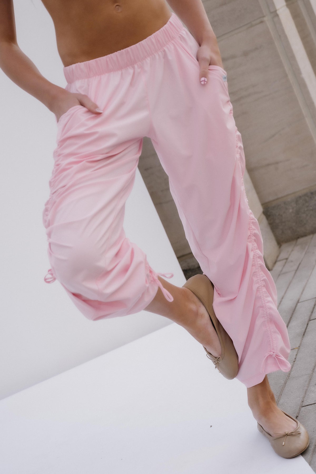 teen, A person wearing light pink wide-leg lounge pants with gathered side details and ruffled trim along the outer edges, paired with beige flats, shown against a light indoor background.