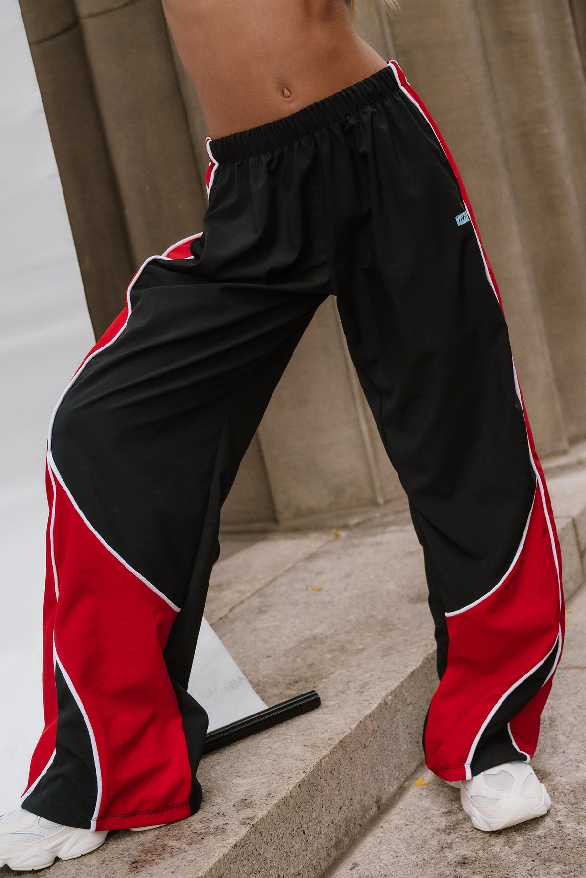 kids, Black wide-leg sweatpants with bold red and white side stripes, worn by a model standing on concrete steps.