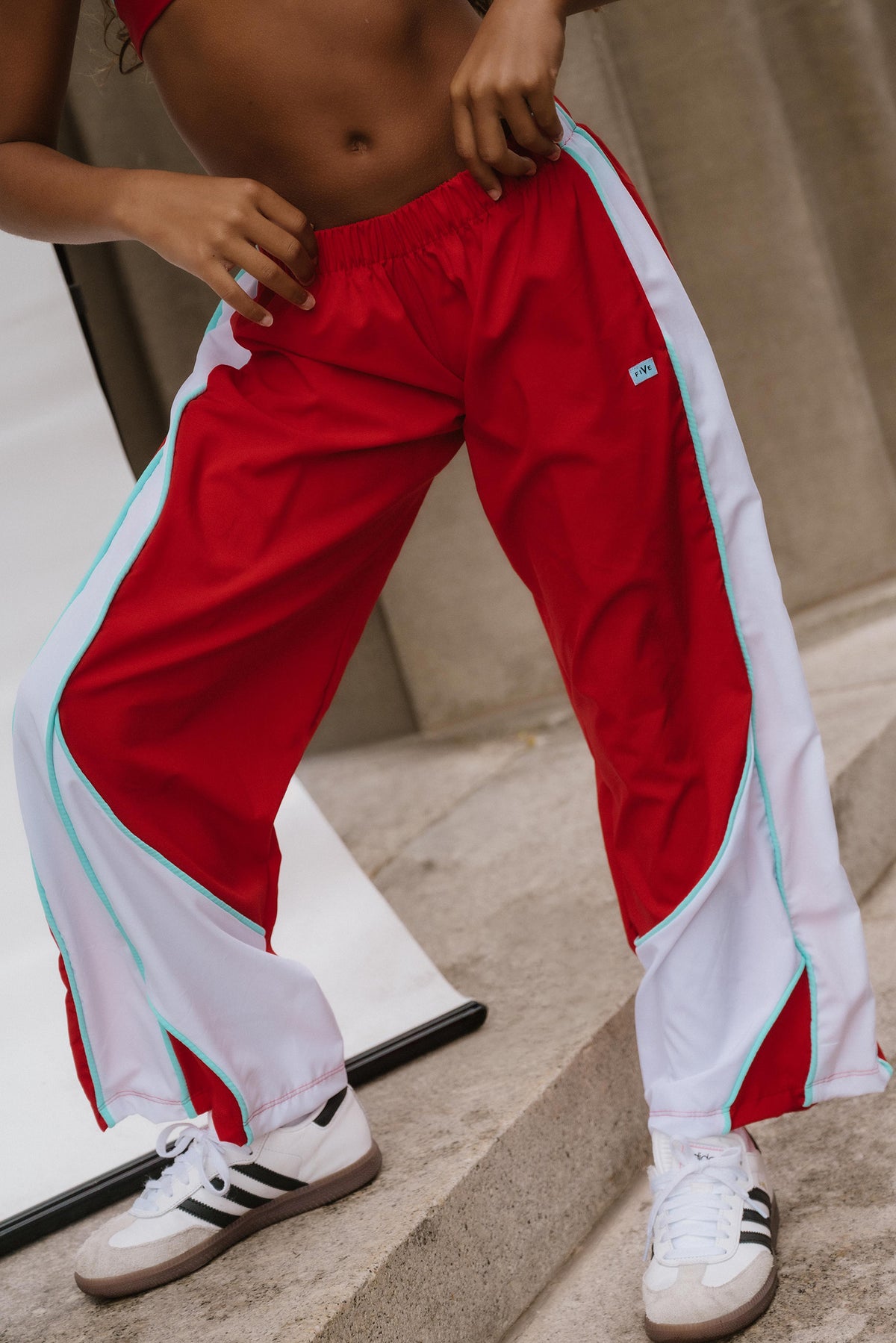 kids, A person wearing red and white athletic track pants with mint green side stripes, paired with white sneakers, standing on concrete steps.