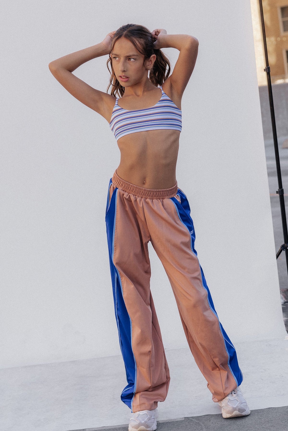 kids, A model posing in a studio setting wearing a striped blue and white sports bra and wide-leg jogger pants with a peach-pink body and blue side panels.