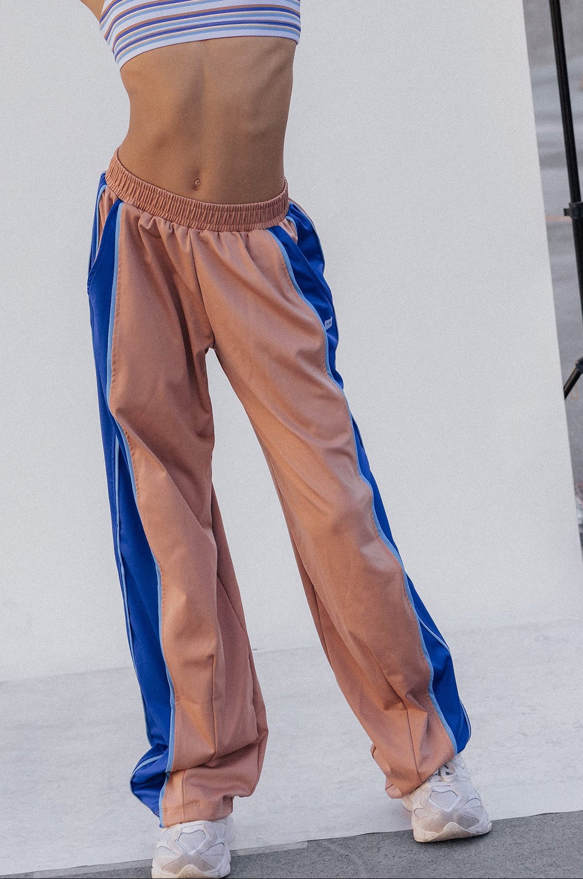 kids, A model posing in a studio setting wearing a striped blue and white sports bra and wide-leg jogger pants with a peach-pink body and blue side panels.