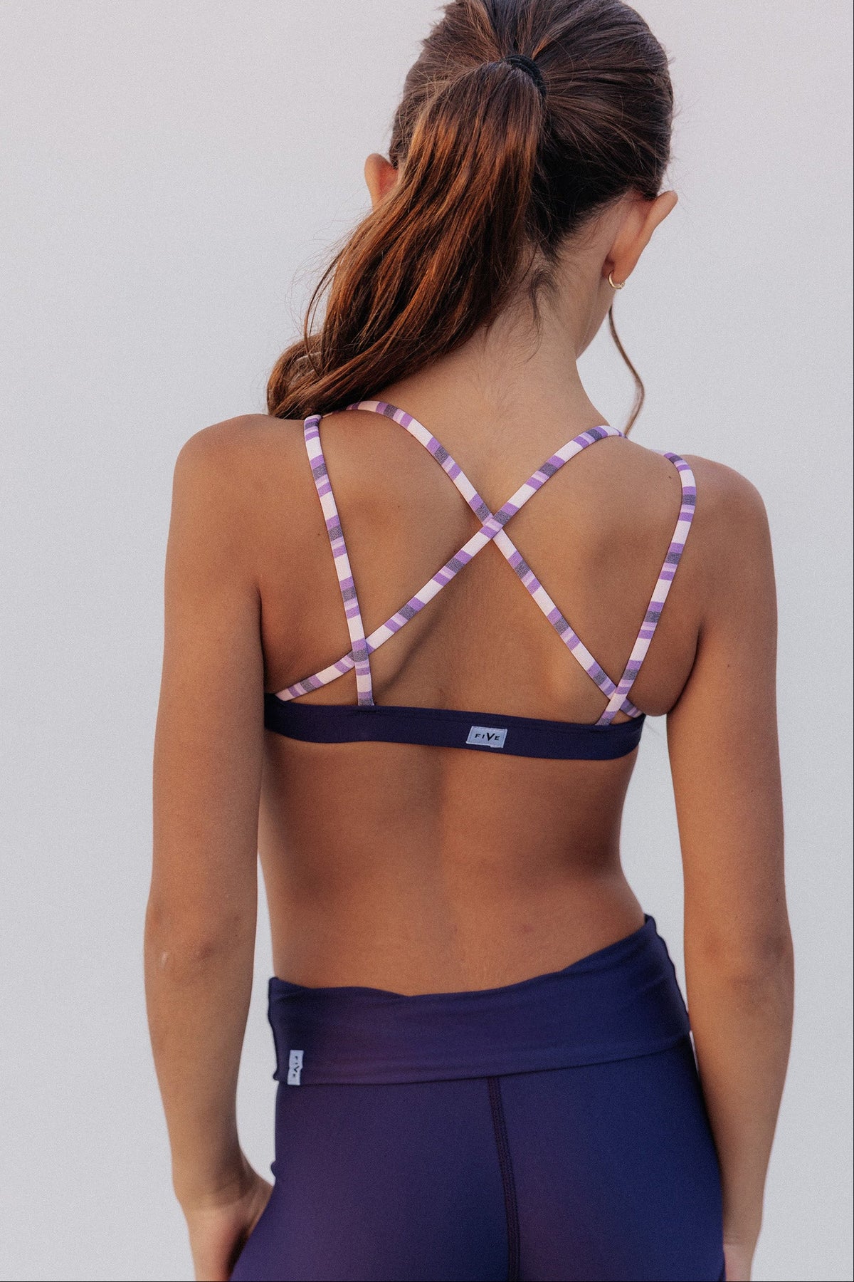 kids, Rear view of a model wearing a purple bra with purple and white checkered crisscross straps, paired with matching purple shorts, against a light gray background.