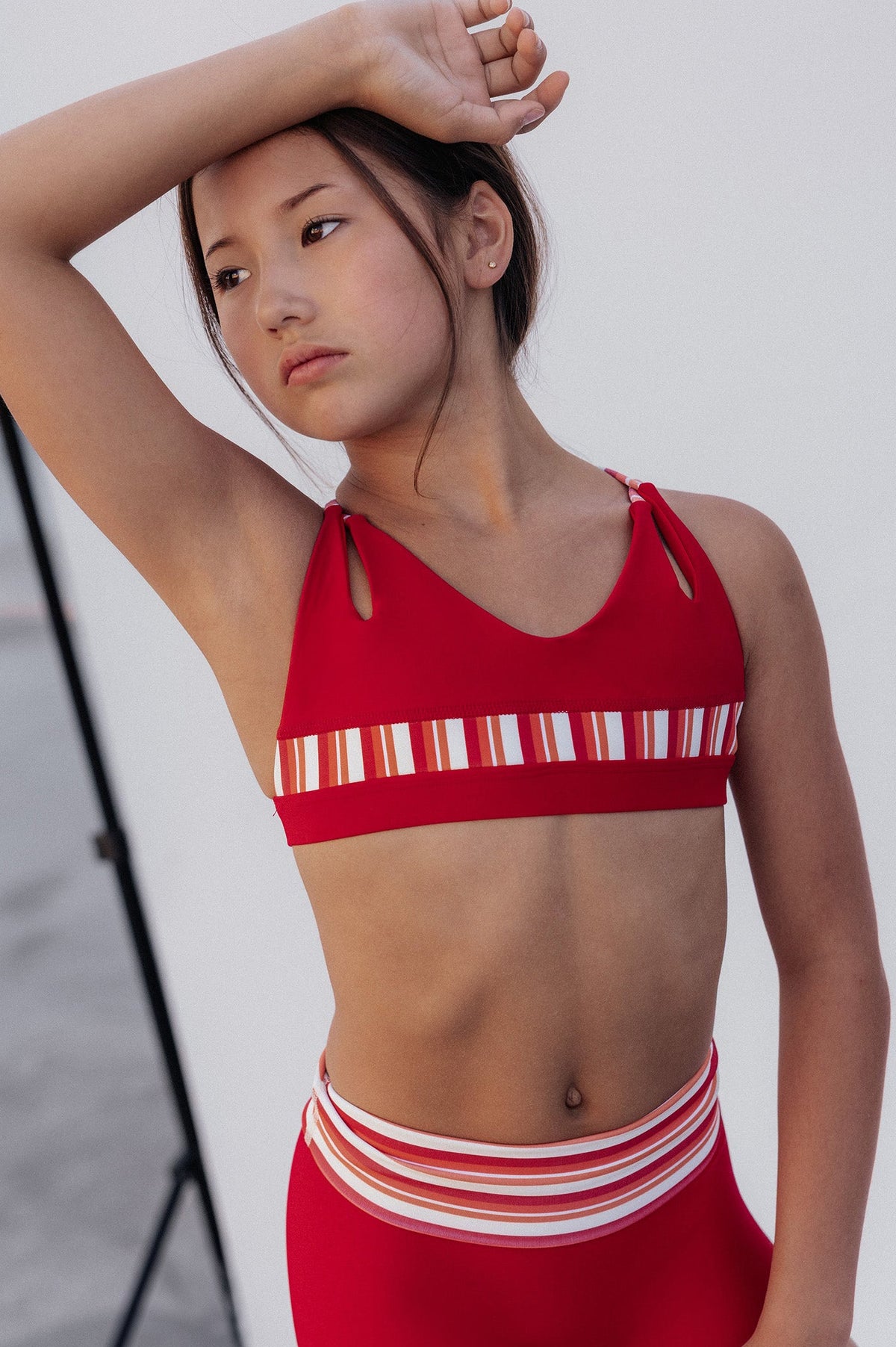 kids, A model wearing a red two-piece athletic set with white and orange striped details, consisting of a sports bra and matching shorts, posed against a white studio background.