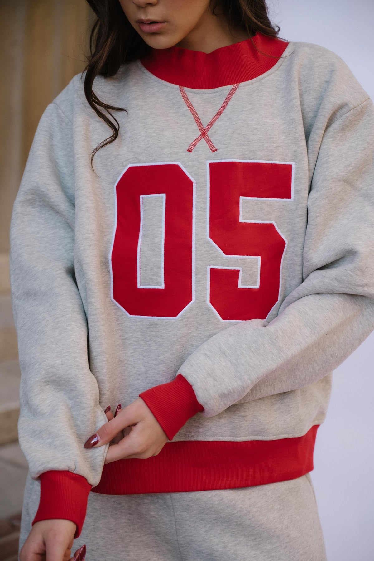 kids, A close-up of a girl wearing a light heather gray sweatshirt with bold red ribbed trim and large red '05' lettering on the front.