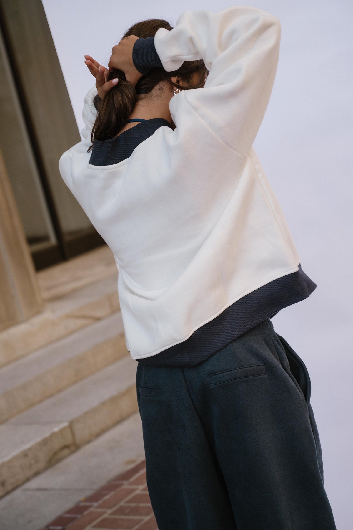 kids, A girl wearing a white cropped sweatshirt with dark navy contrast panels on the collar, cuffs, and hem, paired with dark navy wide-leg pants, shown from behind in an outdoor setting.