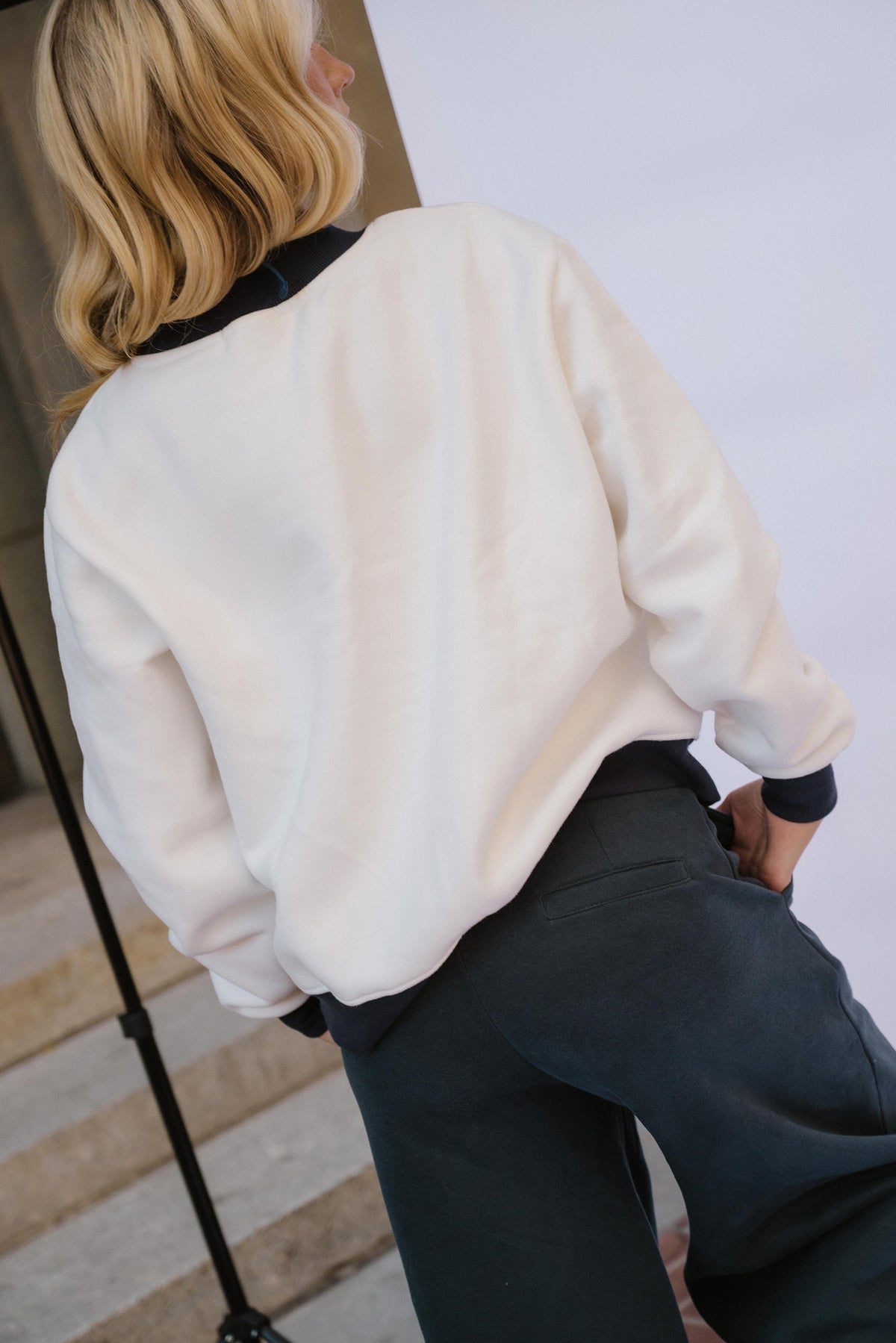 teen, A teen shown from behind wearing a cream-colored long-sleeve sweatshirt with navy ribbed collar, cuffs, and hem, paired with navy pants.