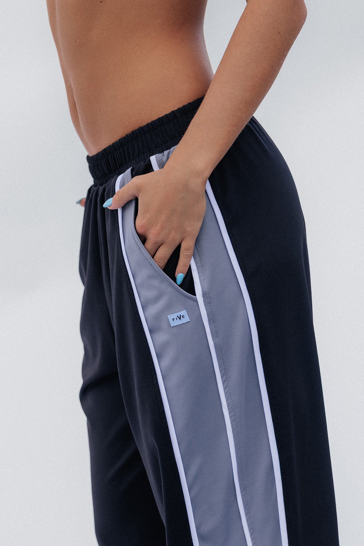 teen, Close-up of a girl wearing black athletic pants with a light gray side panel and white piping, shown from the waist down against a light gray studio background.