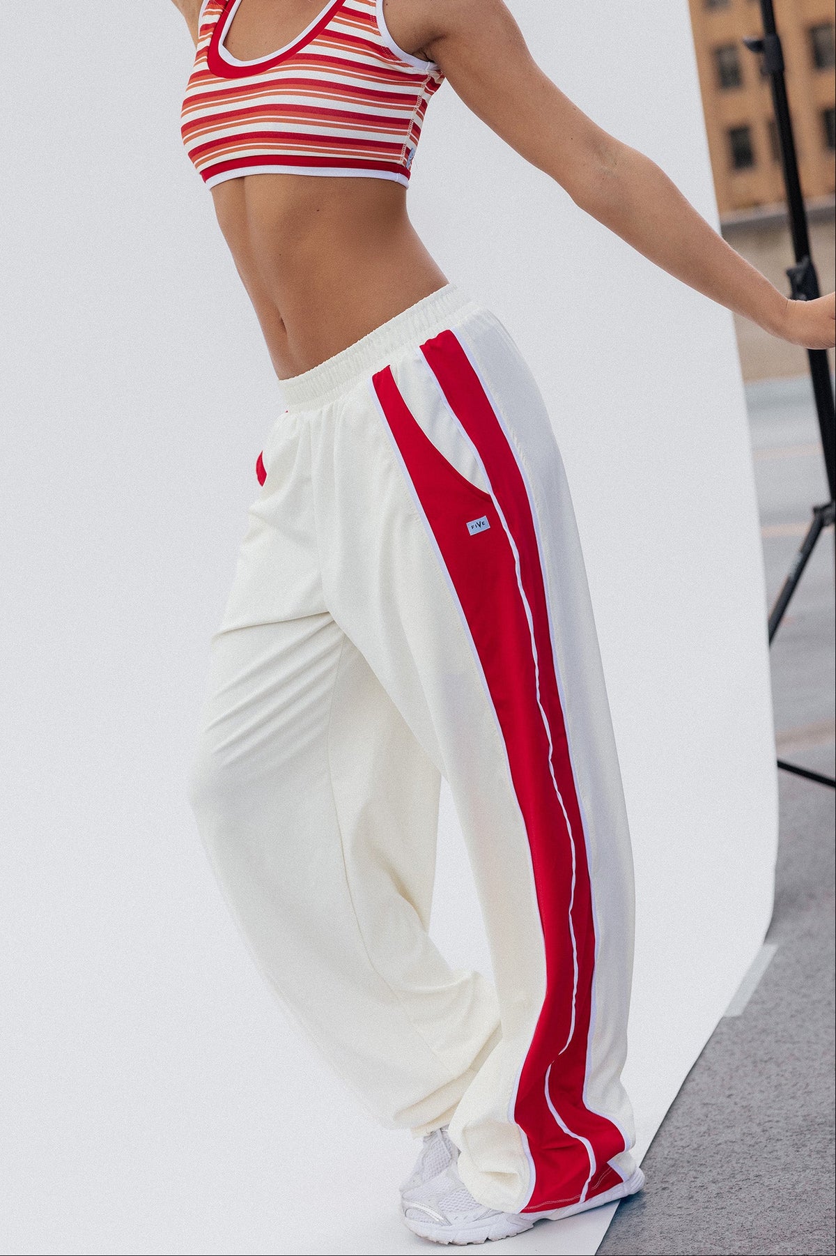 teen, girl modeling a two-piece outfit consisting of a red and white striped crop top and cream track pants with bold red side stripes, photographed in a studio setting.