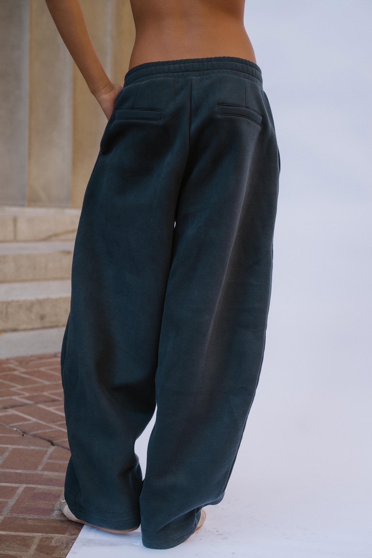 kids, A girl shown from the back wearing very wide-leg navy sweats, standing outdoors near stone steps and a white wall.