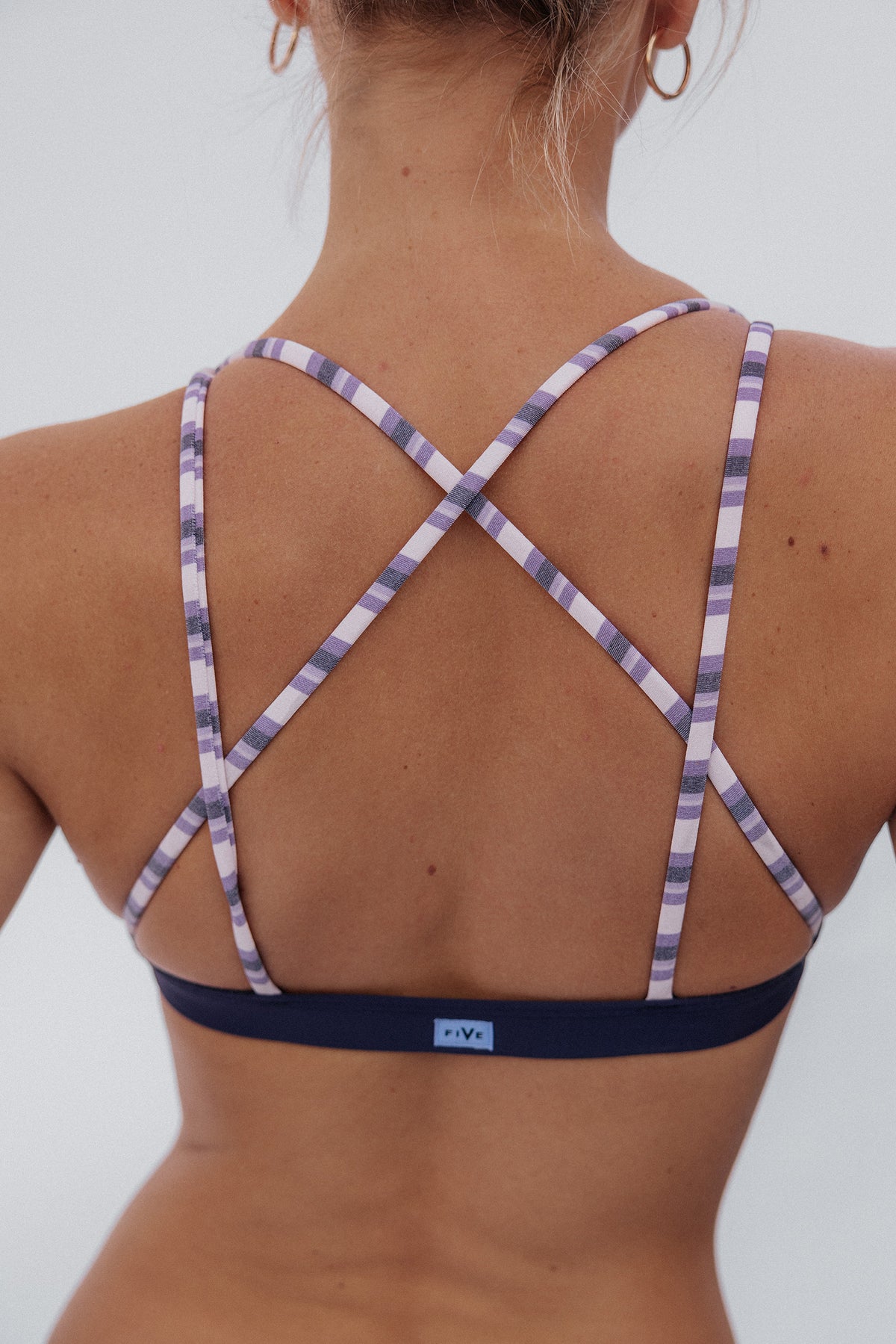 women, Back view of a woman wearing a sports bra with a purple underband and wide shoulder straps featuring a purple and white striped pattern.