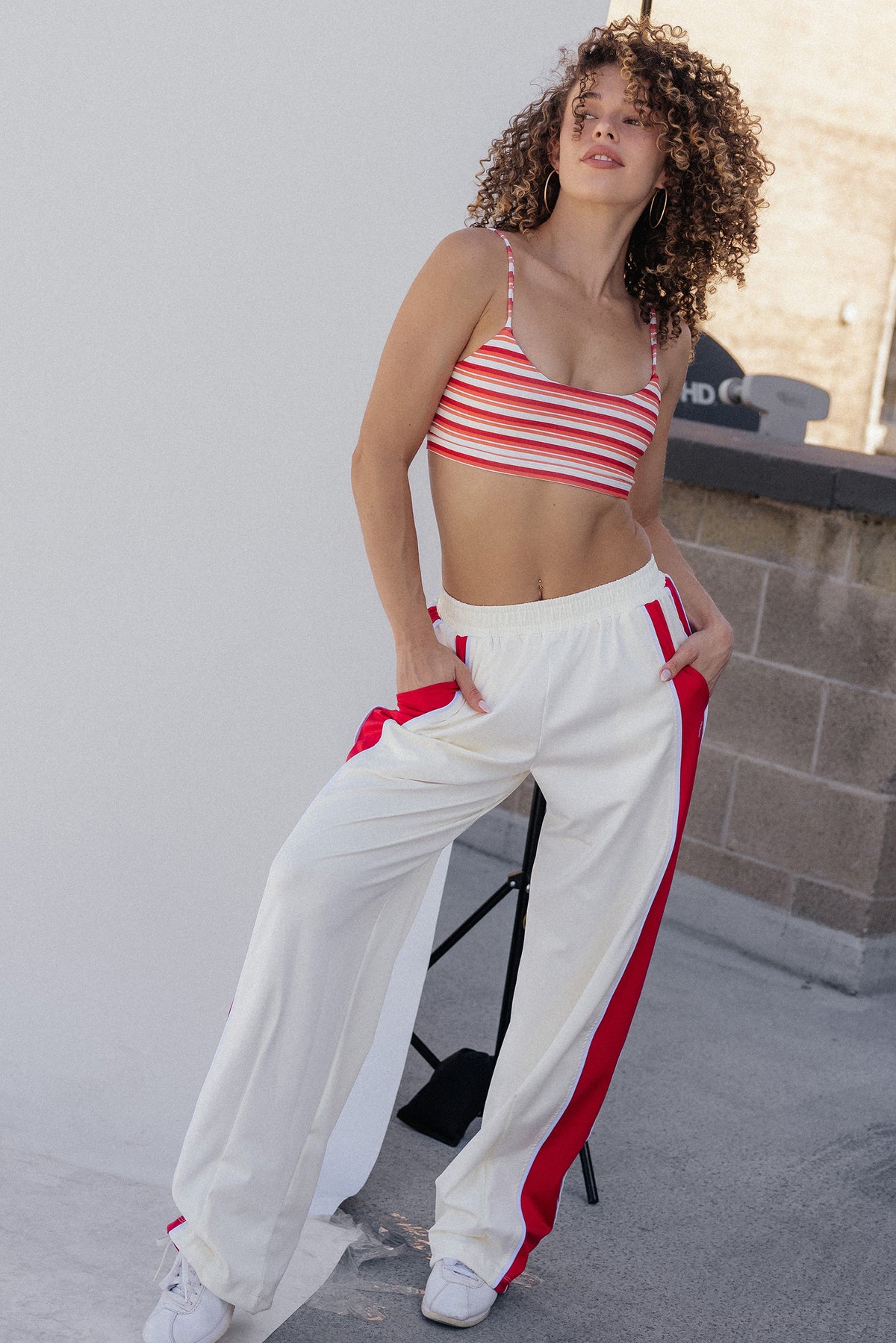 women, A woman modeling a red and white striped crop top and matching red-and-white striped wide-leg sweatpants, standing on a rooftop against a light wall.