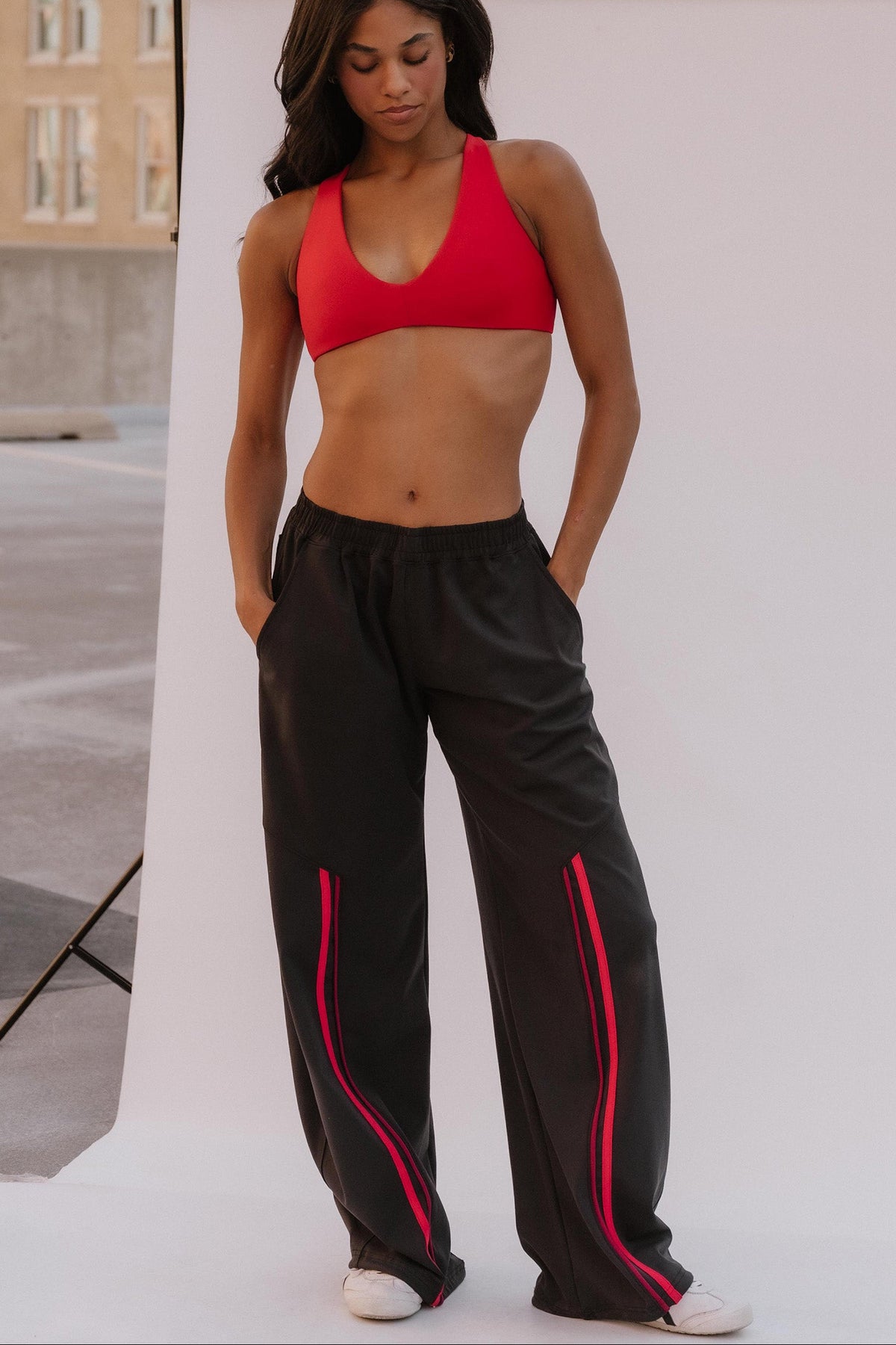 teen, wearing a black pant with red stripe and a red sports bra on a white background.