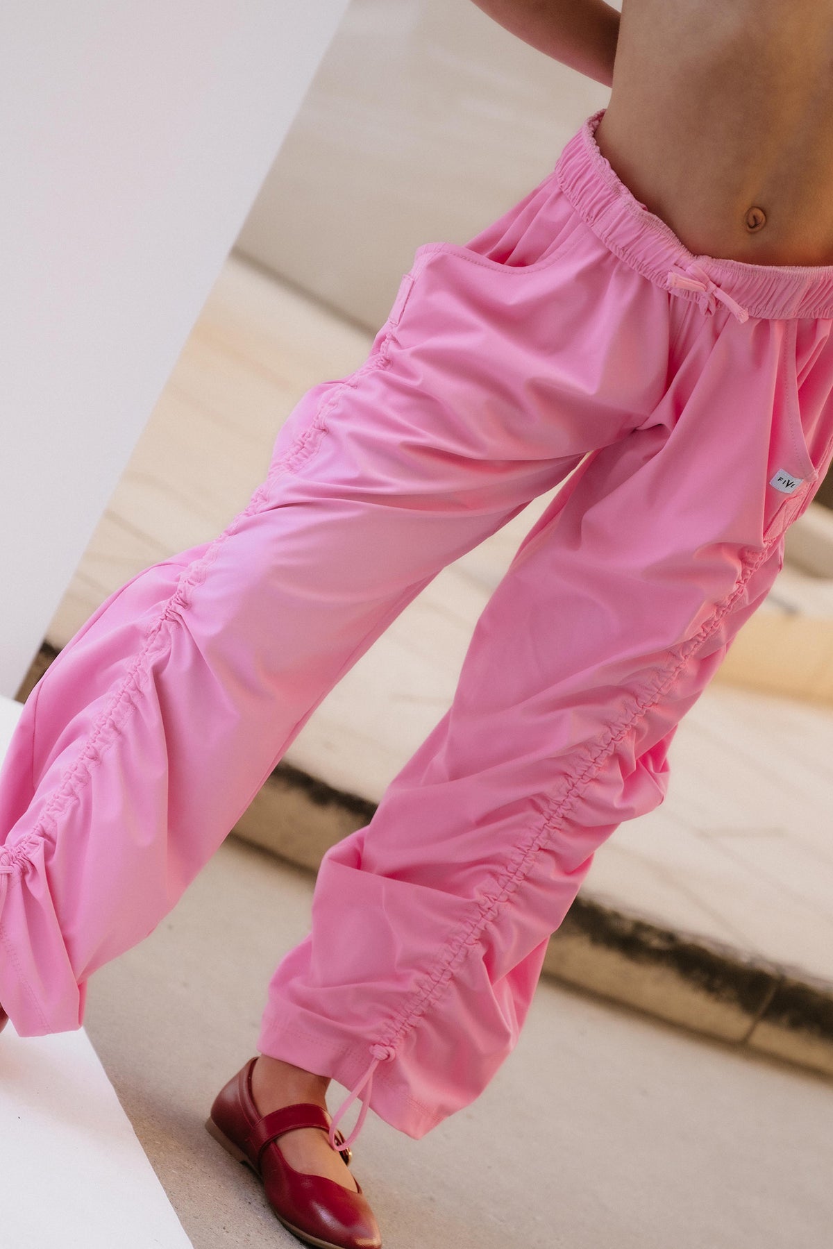 kids,  A close-up of a child wearing bright pink ruched pants with gathered ruffle details along the sides and hems, paired with dark red Mary Jane shoes.