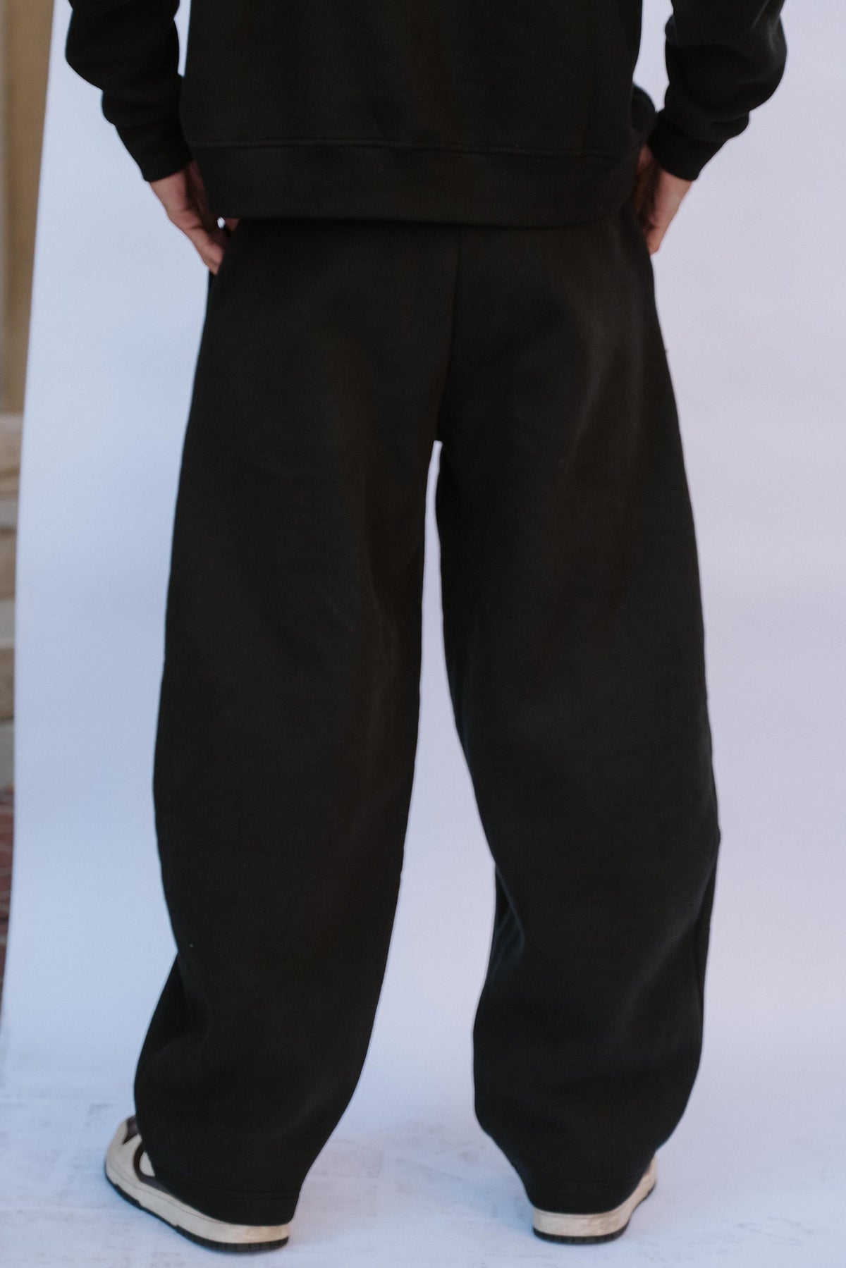 mens, A person shown from the back wearing loose black sweatpants and a black sweatshirt, standing against a plain light background.