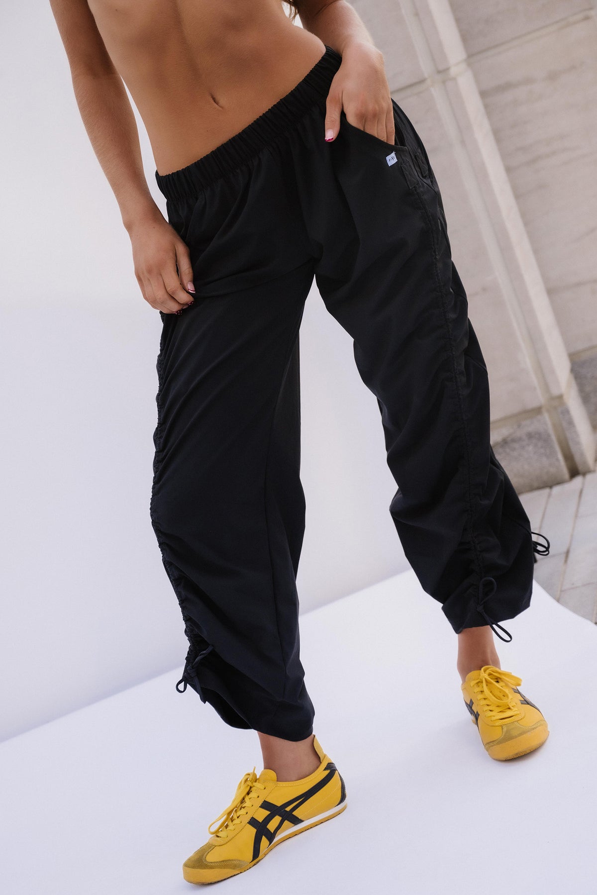 teen, A model wearing black cargo jogger pants with drawstring ankle cuffs and yellow sneakers, shown from the chest down in a studio setting.