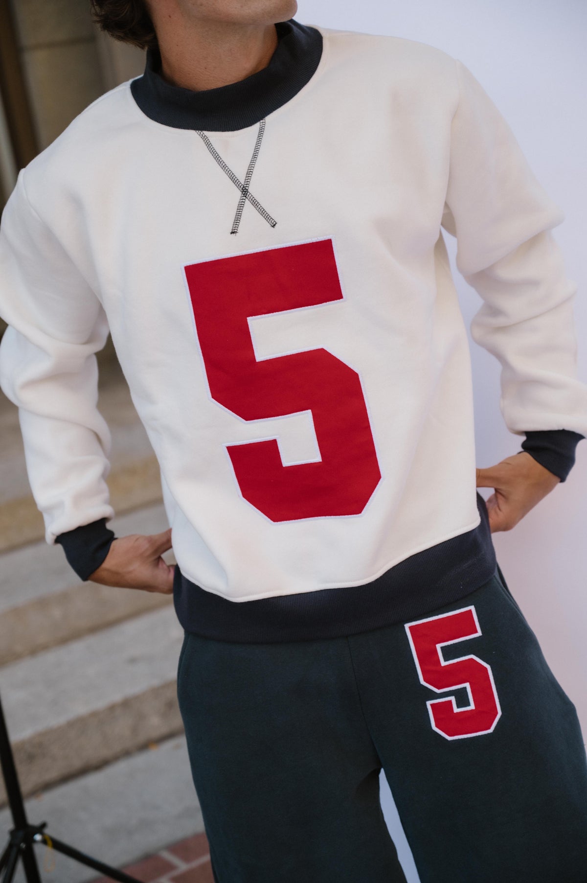 mens, A person wearing a cream long-sleeve sweatshirt with a large red number 5 on the front, paired with dark navy sweatpants featuring a smaller matching red and white number 5 on the thigh.
