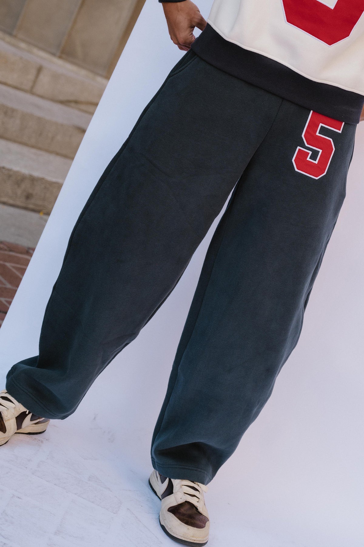 mens, A person wearing oversized dark charcoal sweatpants with a red and white number 5 on the thigh, paired with a white and red top and beige sneakers.