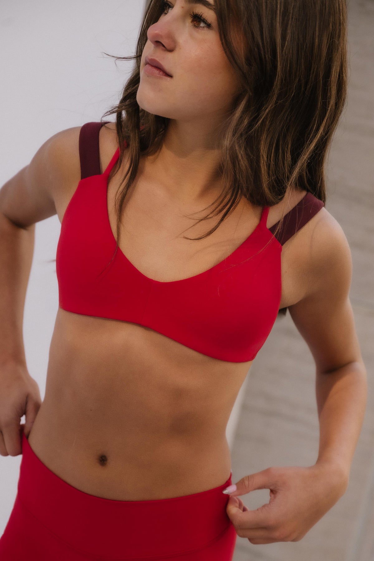 teen, A teen wearing a bright red sports bra and matching high-waisted leggings, shown from the chest down against a light neutral indoor background.