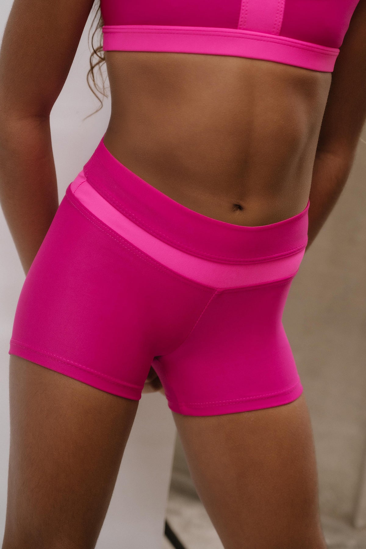 kids, A close-up of a model wearing bright pink athletic shorts with a contrasting lighter pink waistband, paired with a matching pink sports bra.