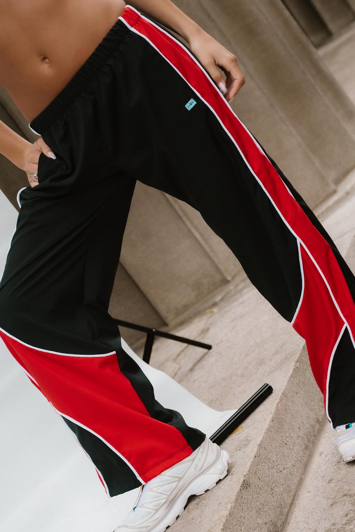 teen, A close-up of a person wearing black track pants with bold red and white side panels, posed on concrete steps.