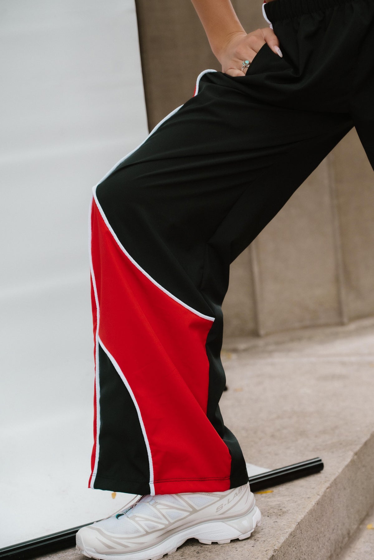 teen, A close-up of a person wearing black wide-leg athletic pants with bold red and white color-block panels on the lower legs, paired with white sneakers.