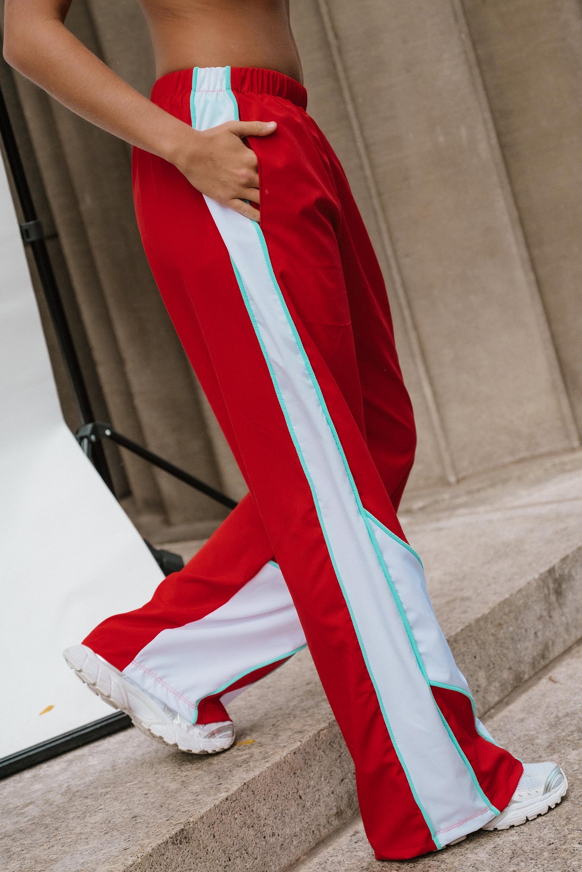 teen, A person wearing red wide-leg track pants with bold white side panels and mint green piping, standing on stone steps.