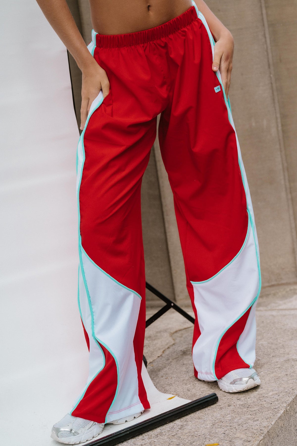 teen, A person wearing red wide-leg track pants with bold white side panels and mint green piping, standing on stone steps.