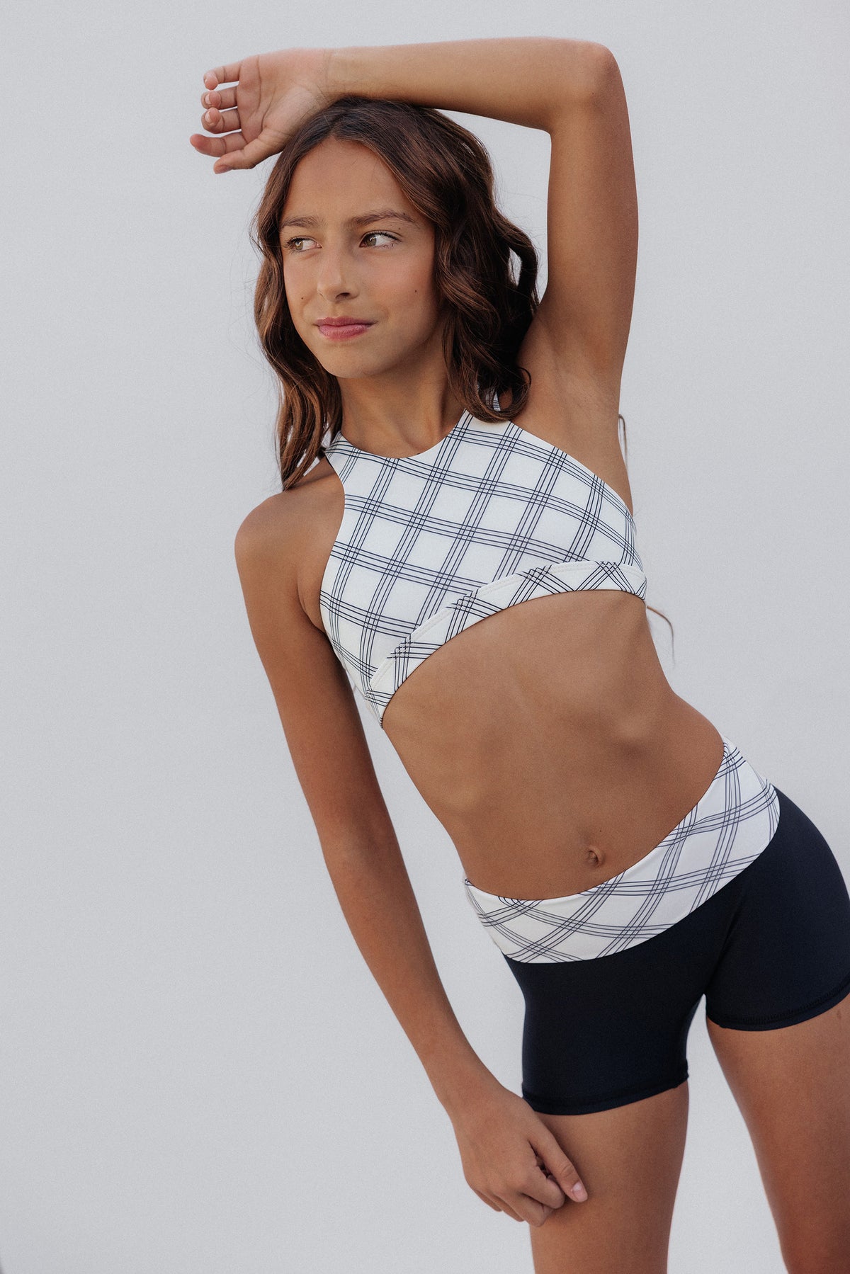 kids, A girl modeling a white and navy plaid halter crop top and matching high-waisted shorts against a light gray studio background.