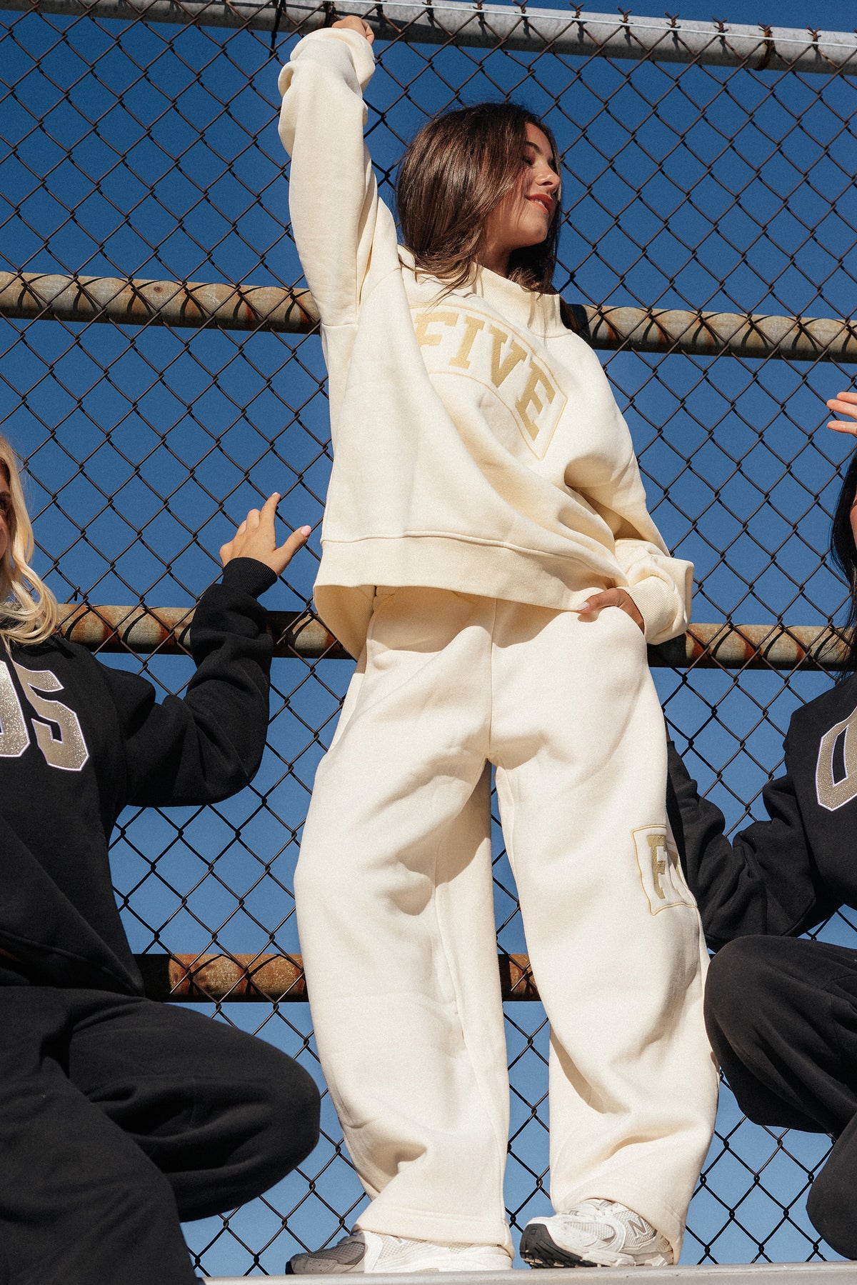 kids, A model wearing a butter-yellow colored sweatshirt and matching sweatpants with 'FIVE' embroidered on the front, posing in front of a chain-link fence under a blue sky.