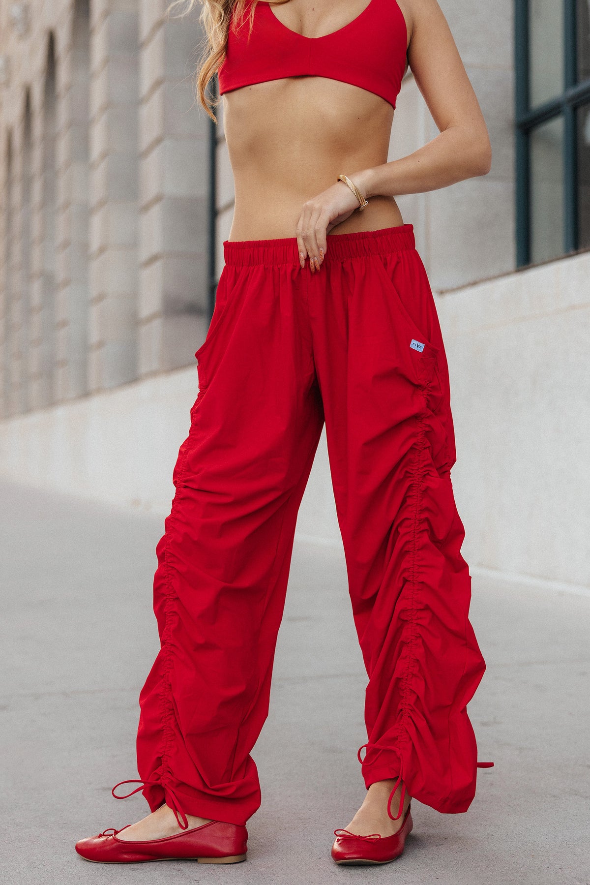teen, a model pose on a neutral building wearing red pants with gather detail on both legs.