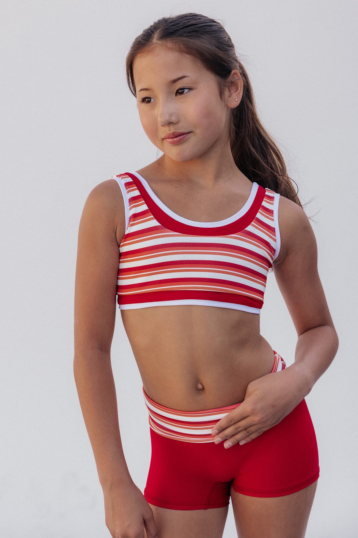 kids, A young girl modeling a red and white striped sports bra and matching red athletic shorts against a plain light gray background.