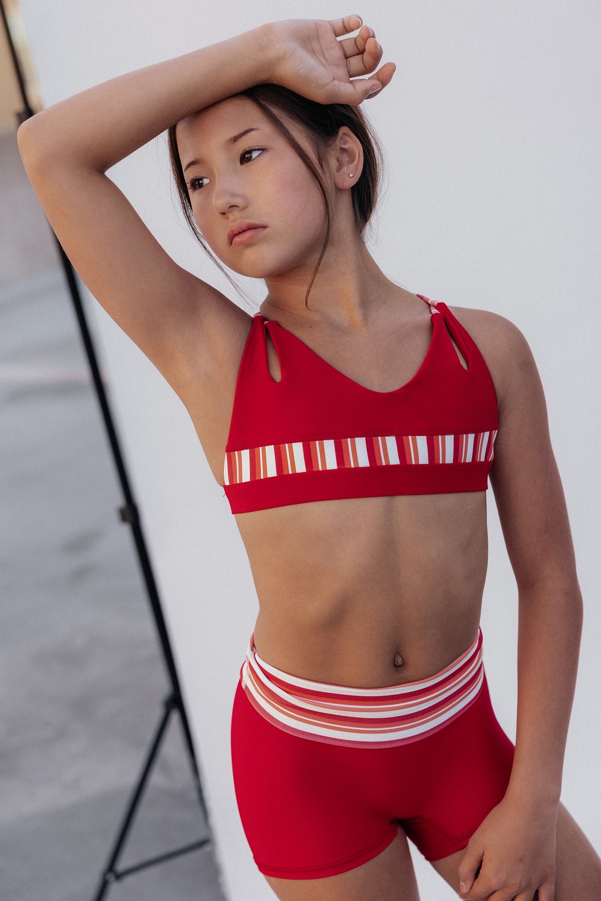 kids, A model wearing a red two-piece athletic set with white and orange striped details, consisting of a sports bra and matching shorts, posed against a white studio background.