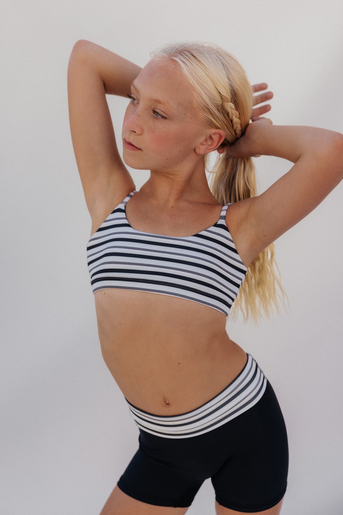 kids, A young blonde girl posing in a black and white striped sports bra and matching striped athletic shorts against a plain light gray background.