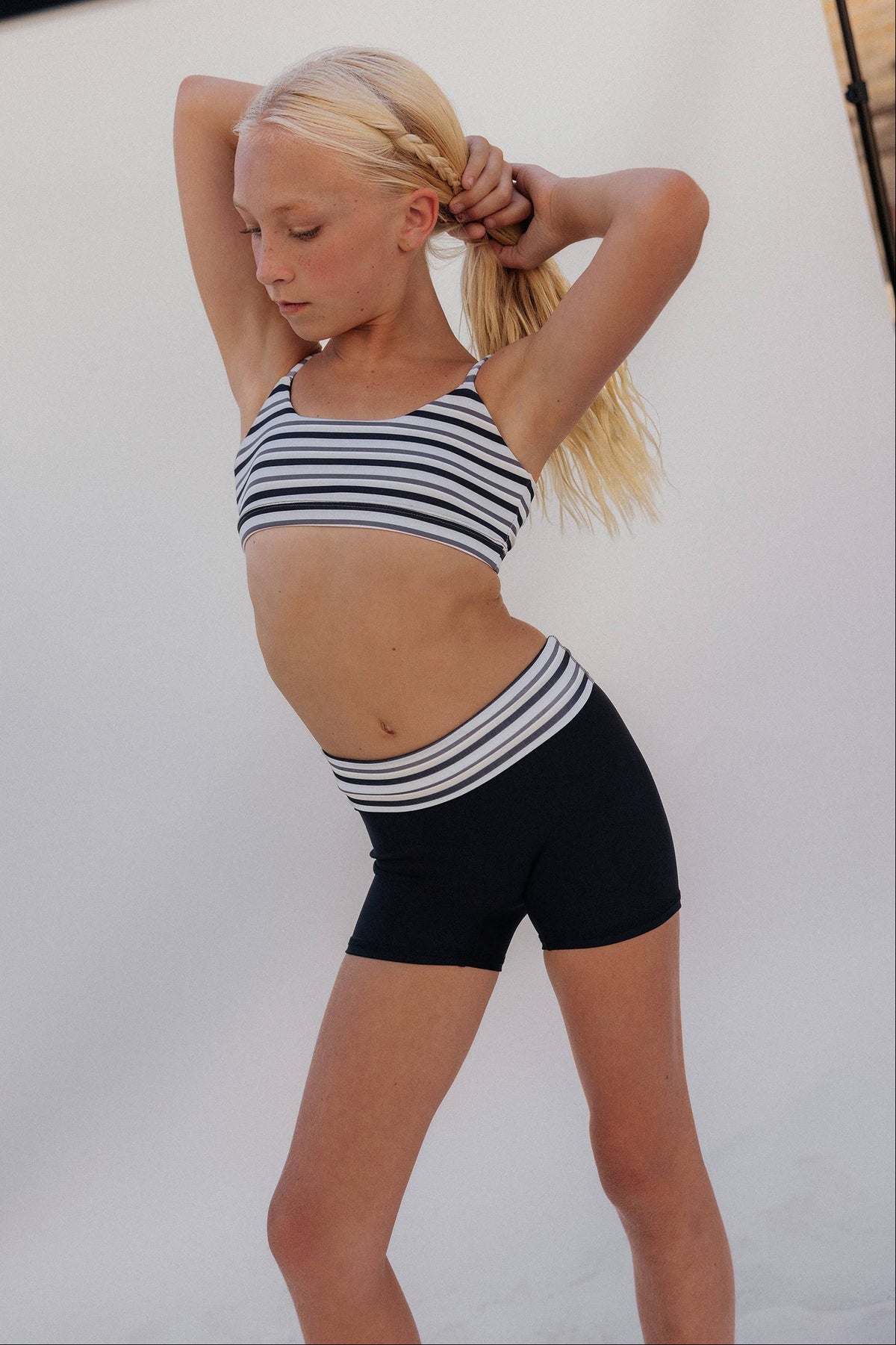 kids, A young blonde girl posing in a black and white striped sports bra and matching black athletic shorts against a white studio backdrop.