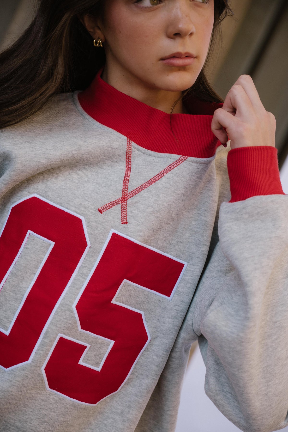 kids, A close-up of a model wearing a light heather gray crewneck sweatshirt with a red mock neck collar, red ribbed cuffs, and a large red number '05' on the front.
