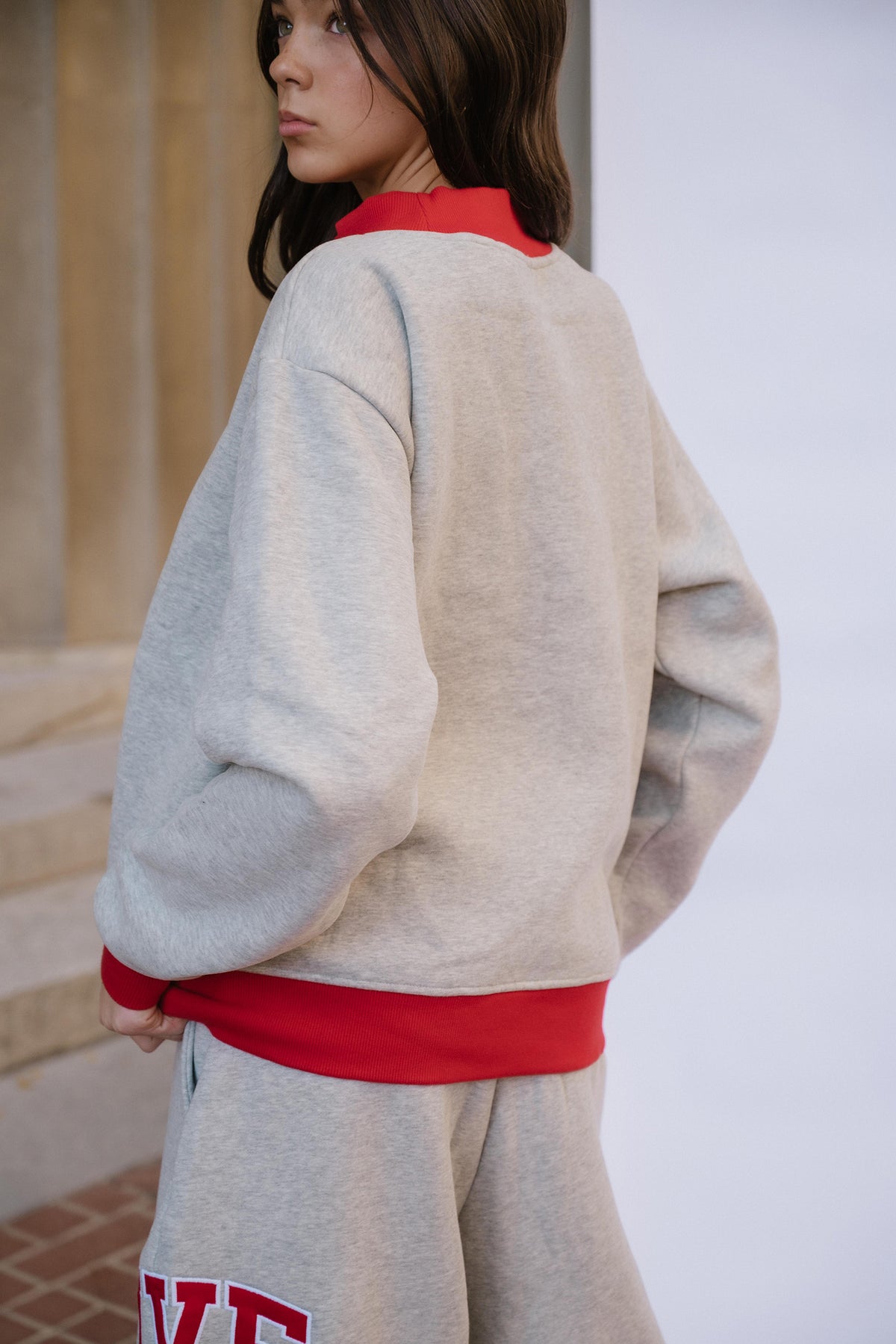kids, A girl wearing a light heather gray sweatshirt with red ribbed trim at the collar, hem, and cuffs, paired with matching gray sweatpants, photographed in an indoor setting.
