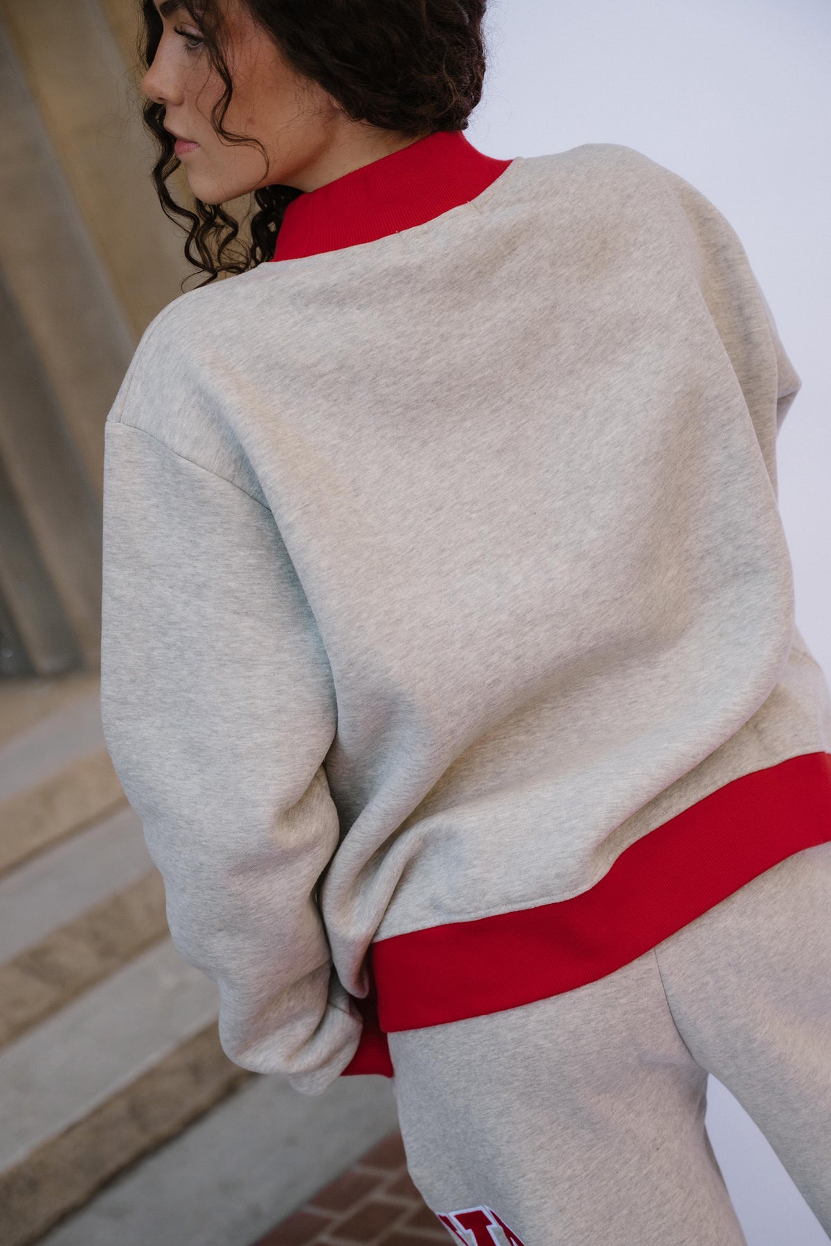 teen, A girl wearing a light heather gray sweatshirt with a bright red ribbed collar and hem, paired with matching gray sweatpants, shown from a side-back angle.