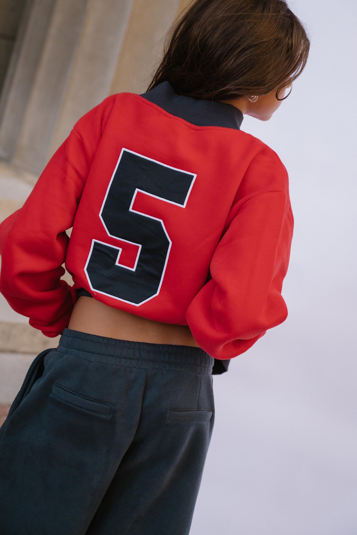 kids, A girl shown from behind wearing a cropped red varsity-style sweatshirt with a large navy number 5 on the back, paired with navy sweat pants.