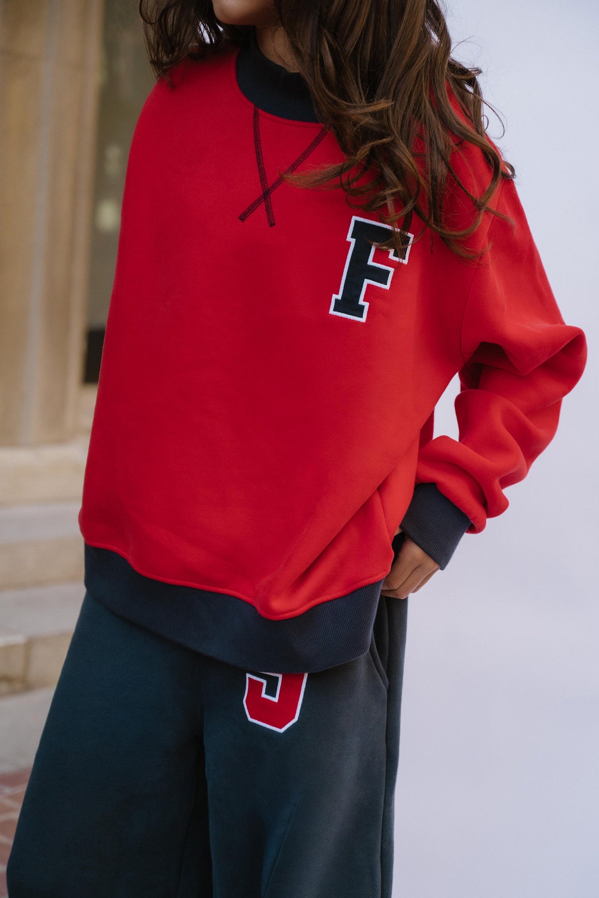 kids, a girl wearing a red crewneck sweatshirt with a large navy and white letter 'F' on the chest, paired with dark navy sweatpants featuring a matching number '5' on the thigh.