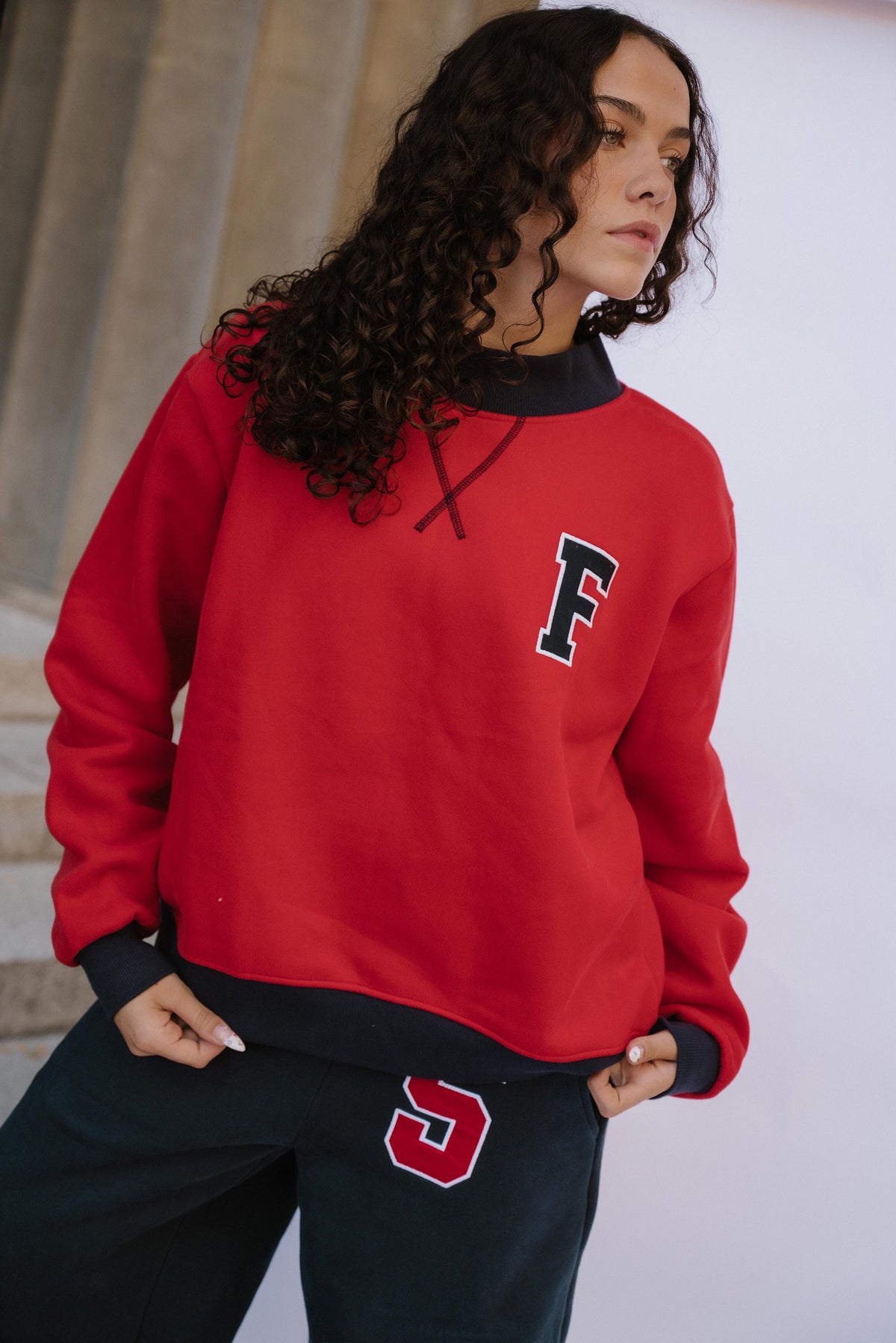 teen, A girl wearing a red sweatshirt with a navy collar and a large letter 'F' on the chest, paired with navy pants featuring a red and white number '5'.