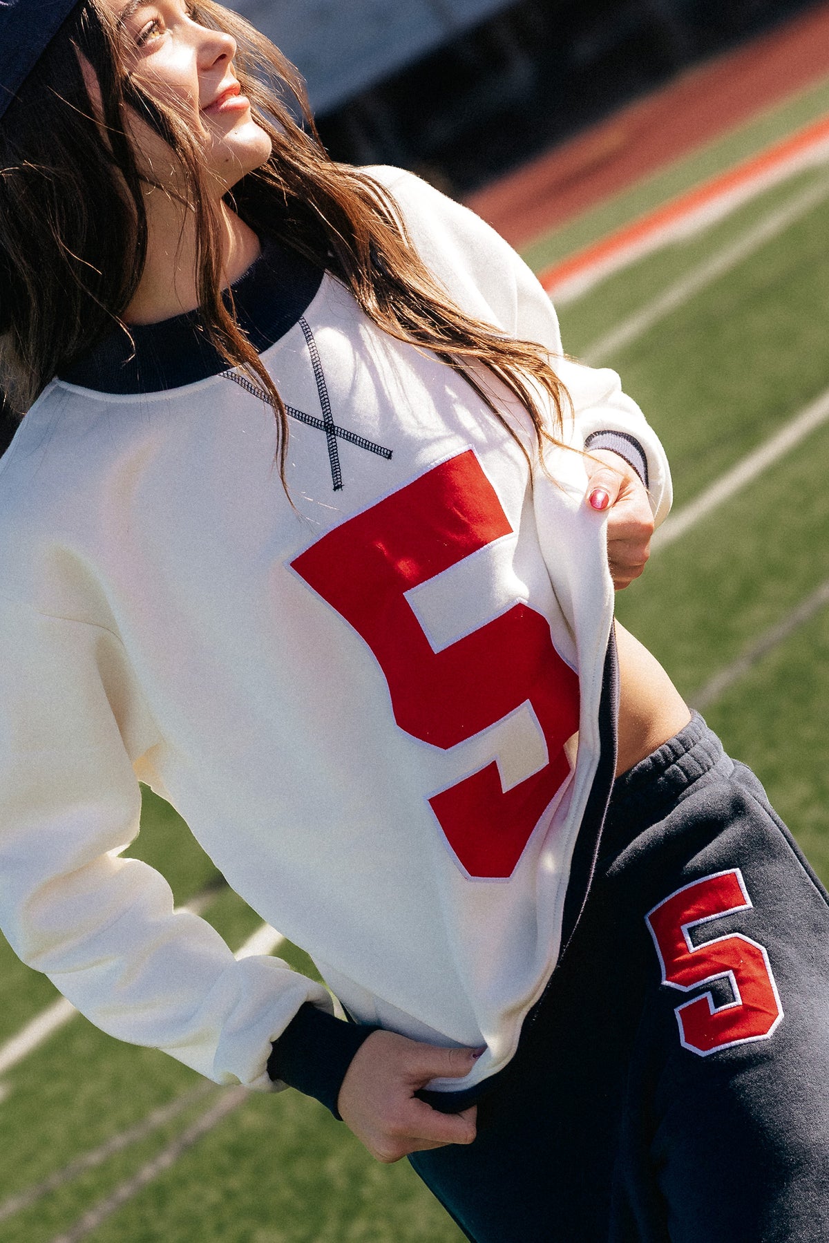 kids, on a football field wearing a cream long-sleeve sweatshirt with a large red number 5 on the front, paired with navy sweatpants featuring a red and white number 5.